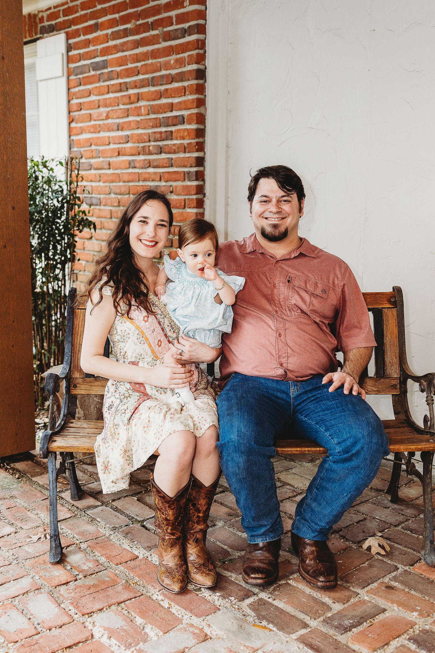 Family sitting together on a rustic brick porch with brown and floral outfits.
