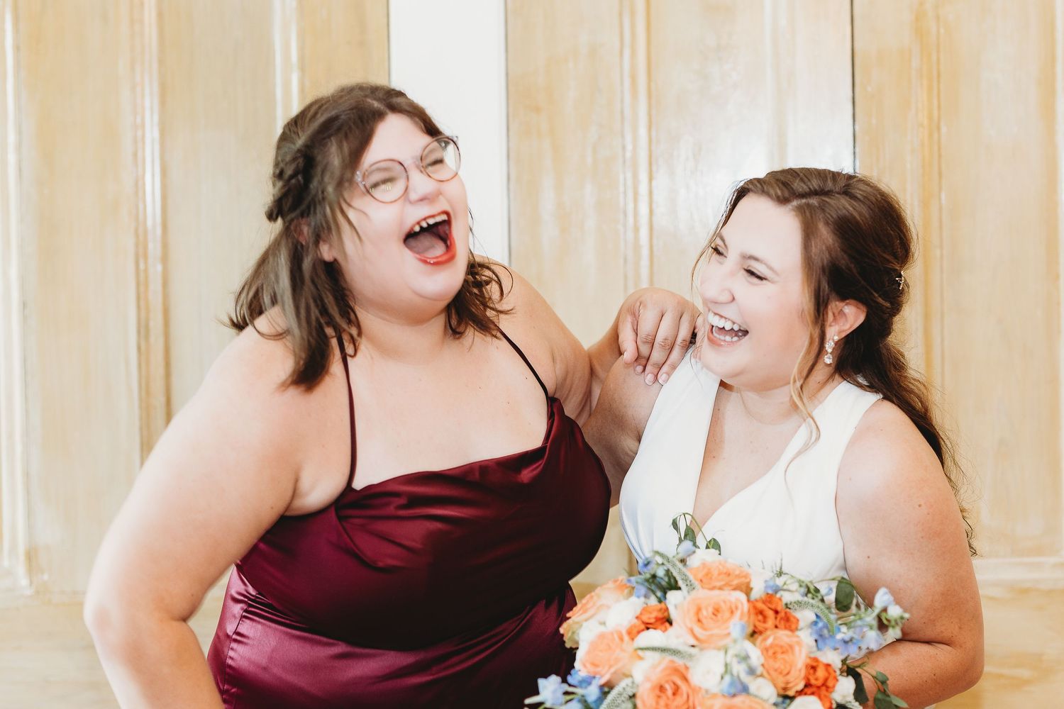 Wedding party members share joyful candid moments in burgundy attire.