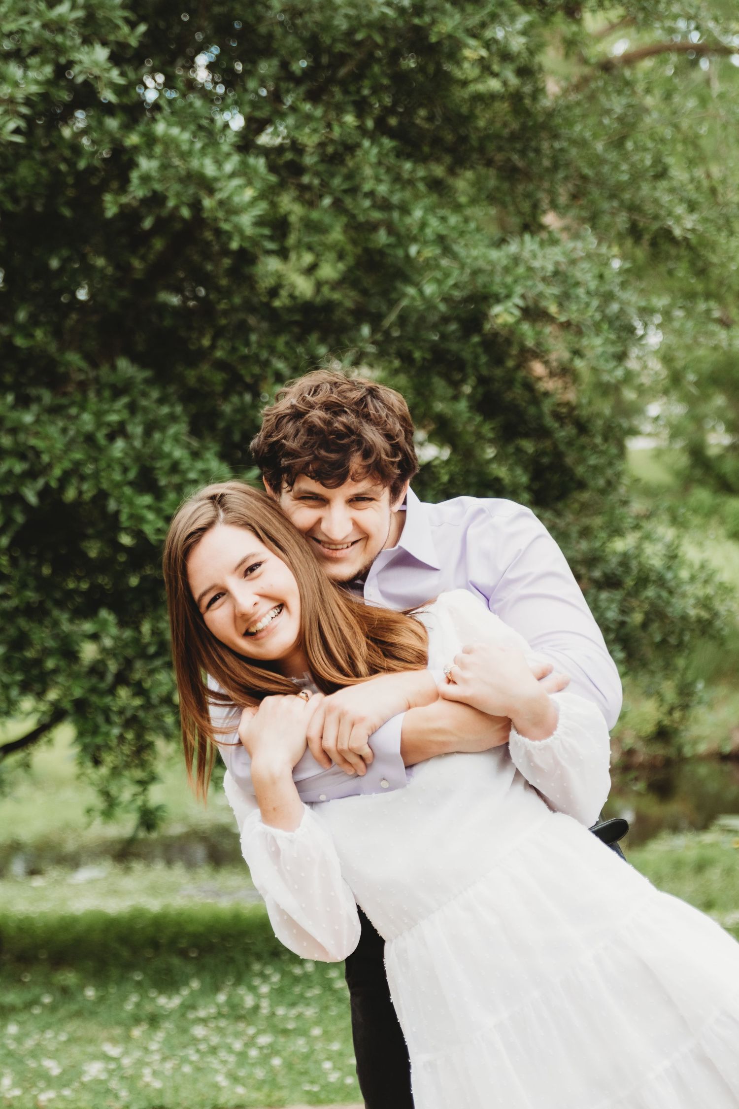 A playful couple in white clothing shares joyful moments together in a sunny outdoor garden setting.