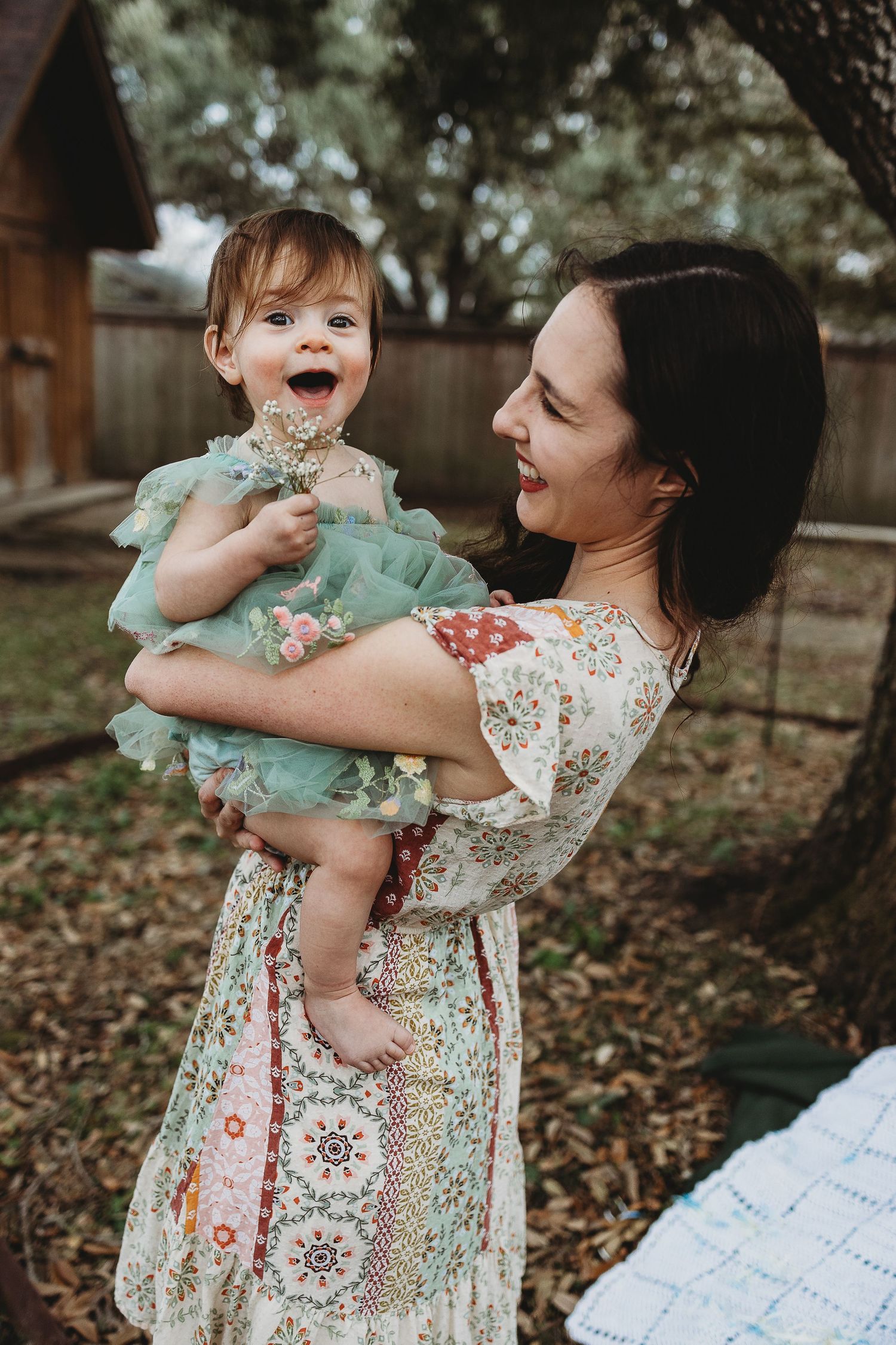 Mother and baby sharing playful moments outdoors in floral and mint green outfits.
