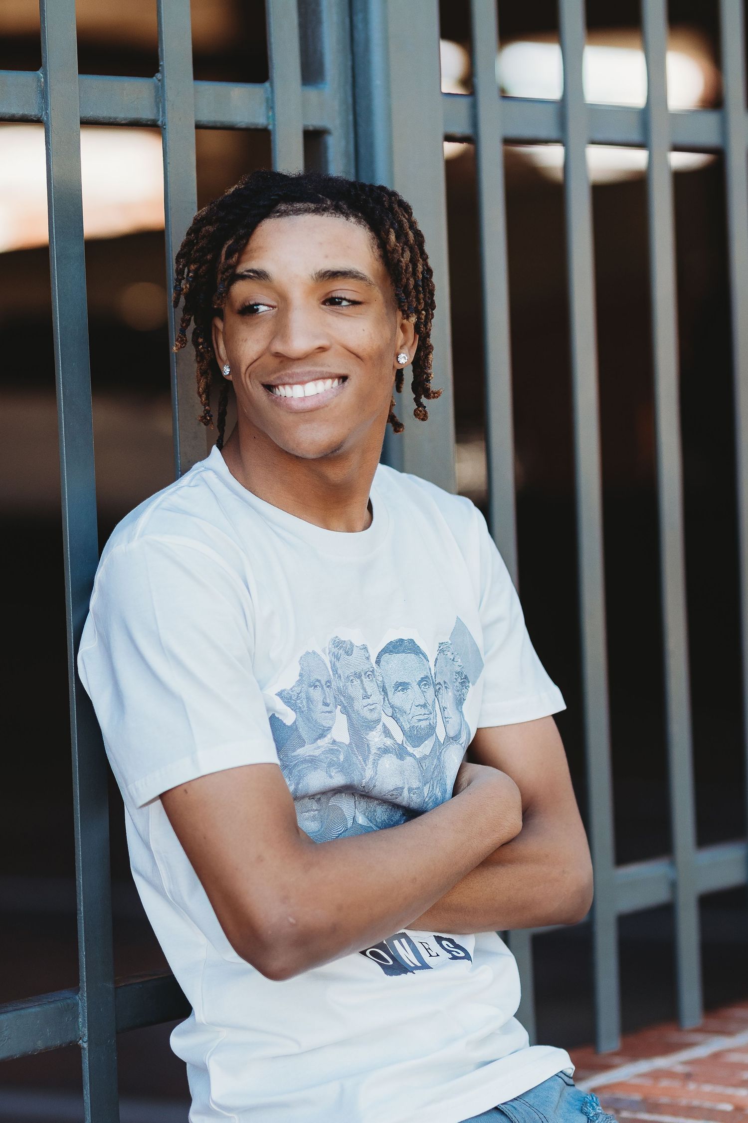 A casual portrait of someone in a white graphic t-shirt leaning against metal railings.