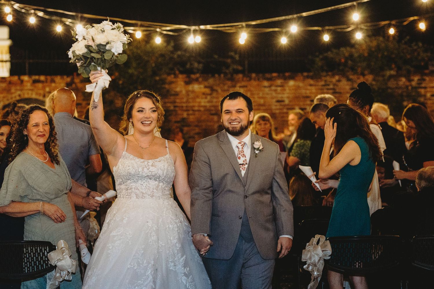 String lights illuminate an evening wedding reception with guests dancing and celebrating.