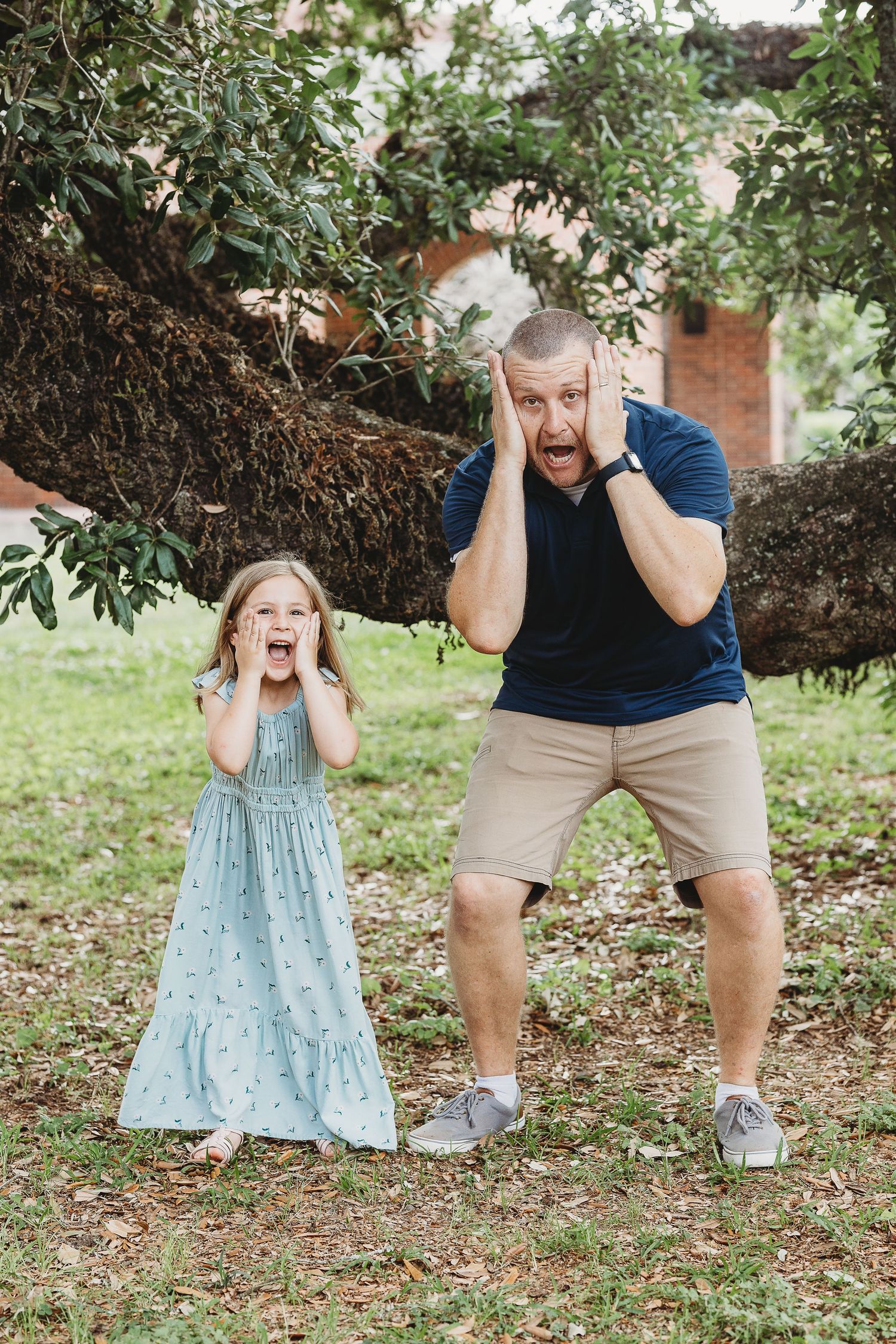 Two people make exaggerated surprised expressions while posing under a tree.