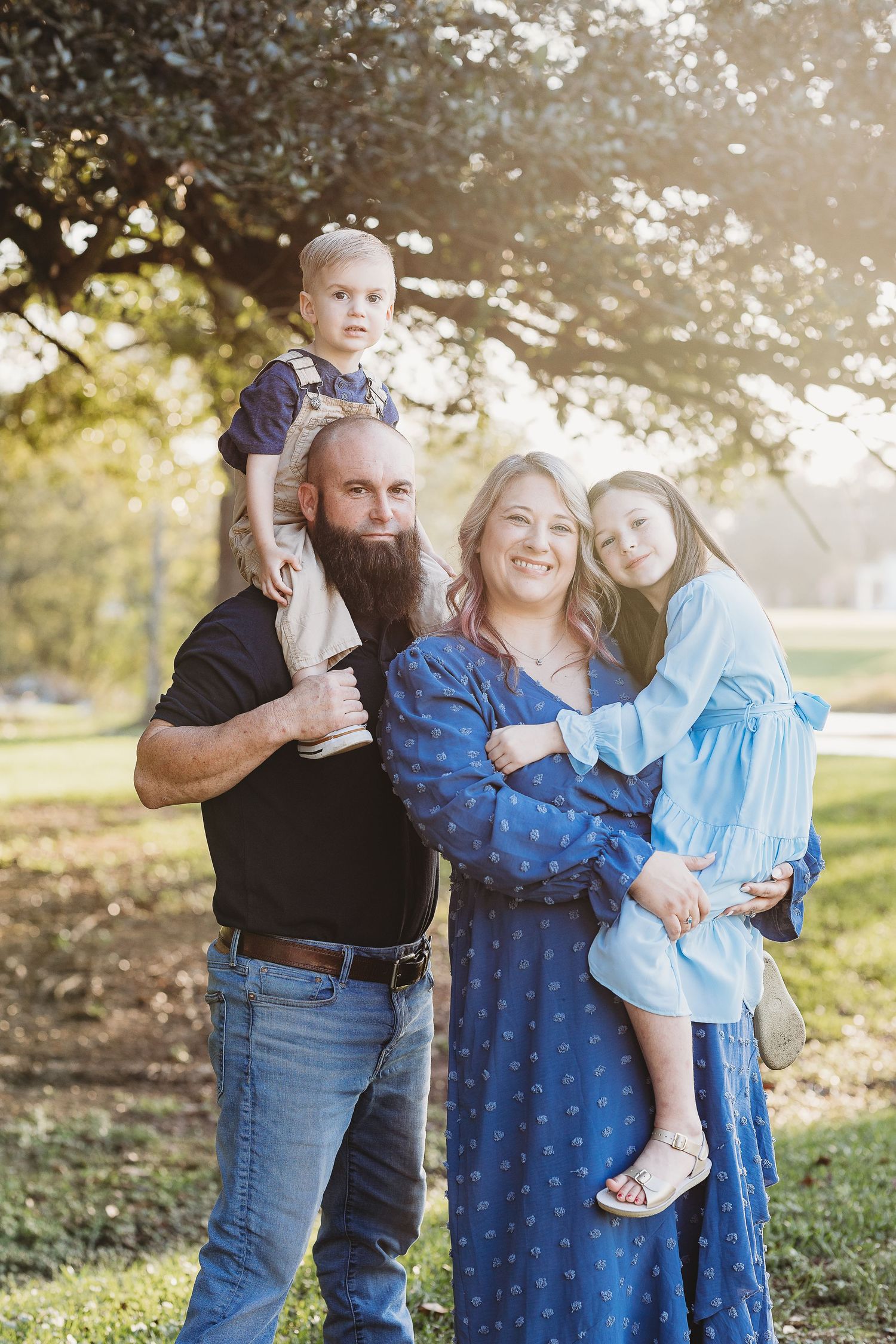 A family of four poses together outdoors in casual attire on a sunny autumn day.
