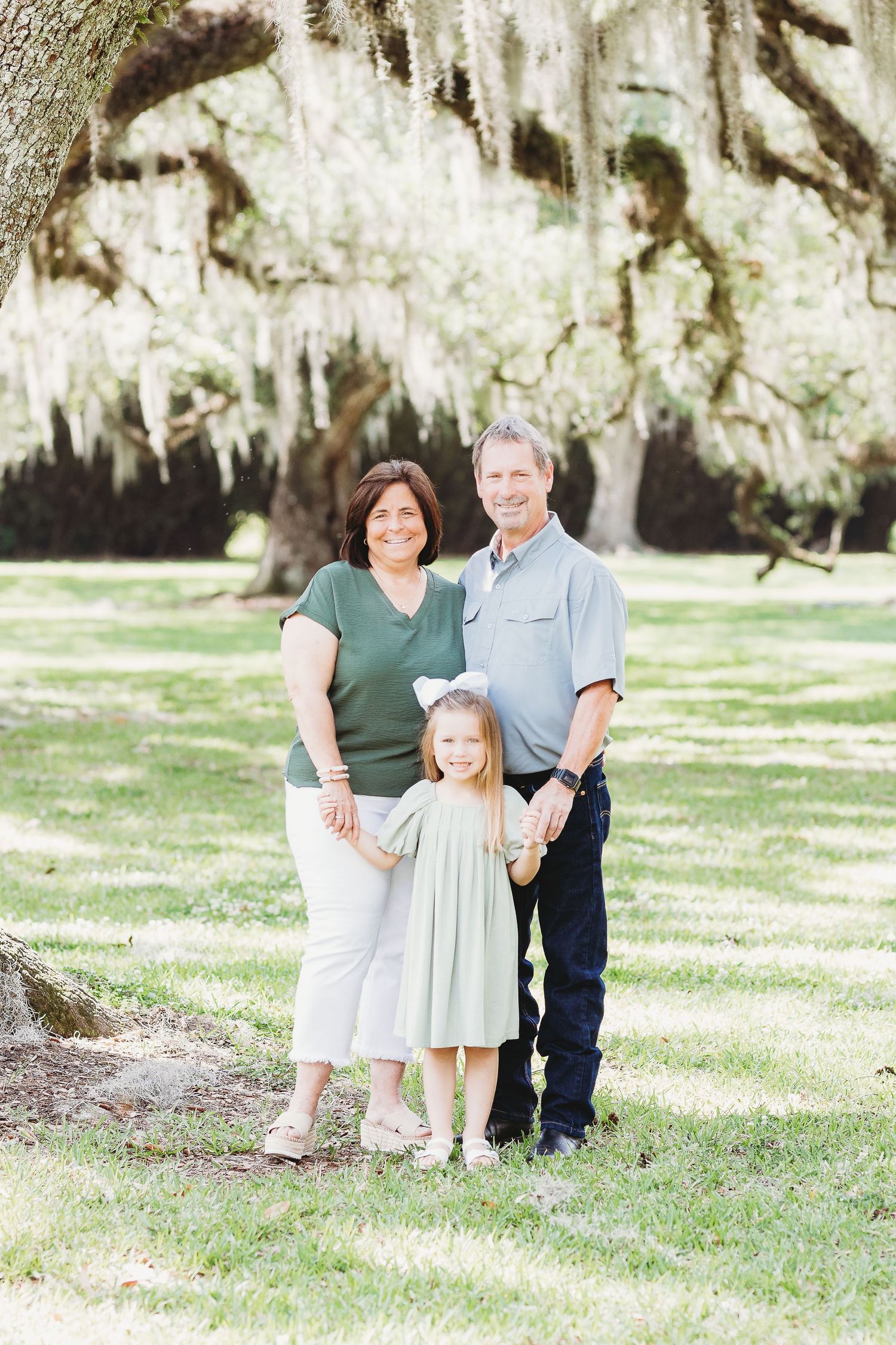 A family poses together under Spanish moss hanging from trees in a sunny outdoor setting.