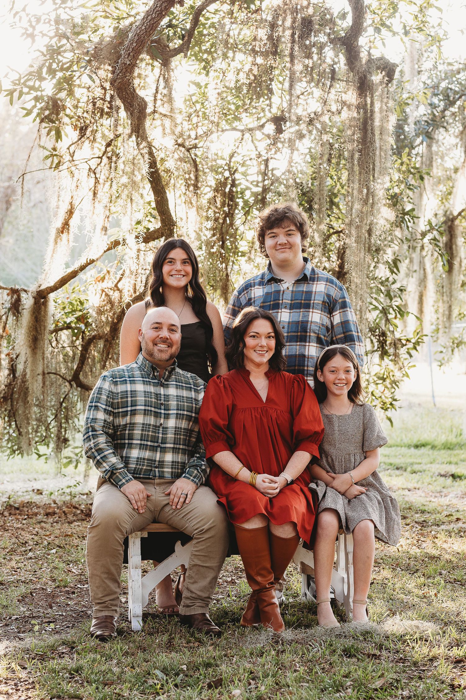Family sitting together on grass with Spanish moss hanging from trees in the background.