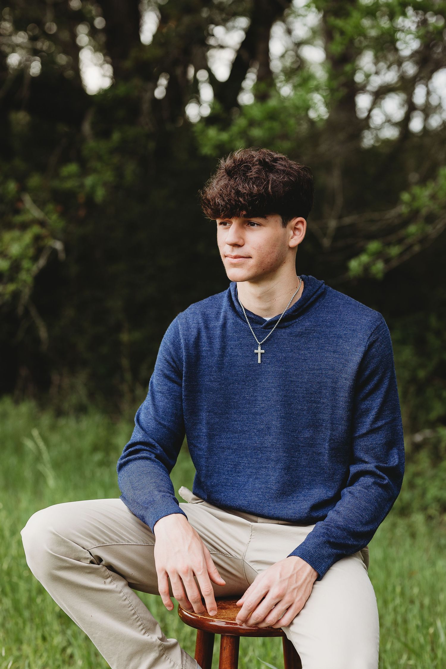 Person in navy sweater sitting outdoors against natural green background.