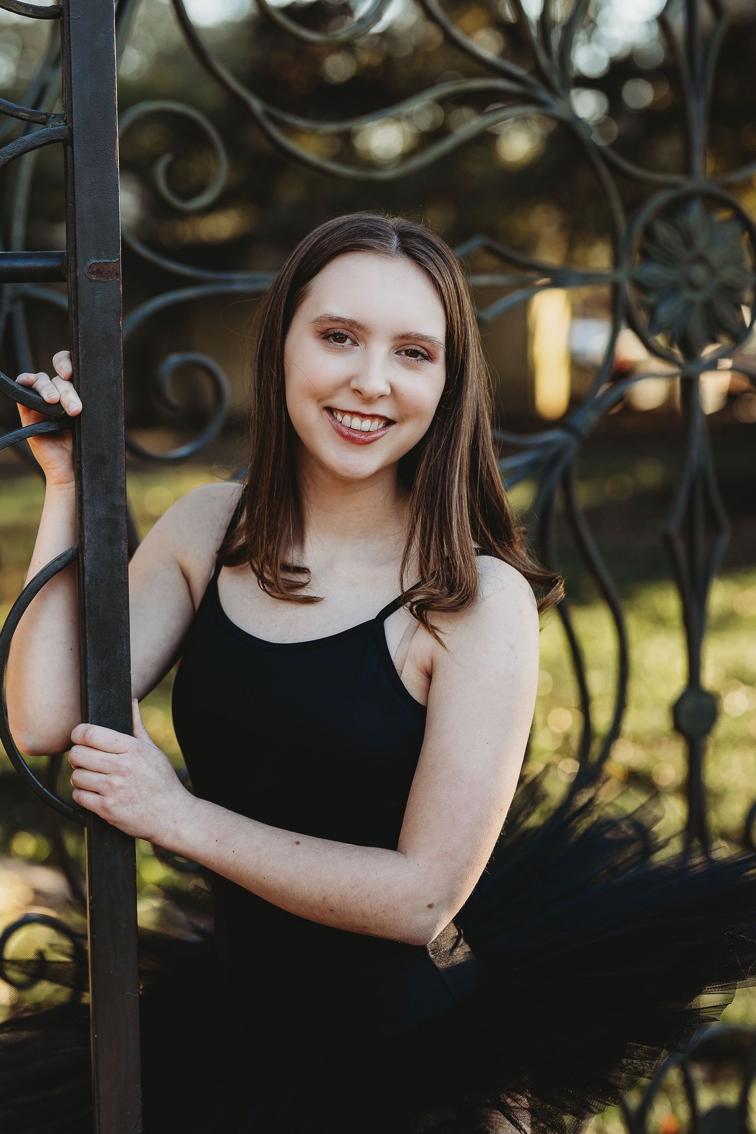 A dancer in black attire poses gracefully against decorative iron gates.