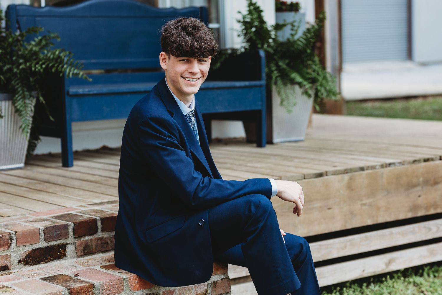 Person in navy suit jacket sitting on brick ledge outdoors.