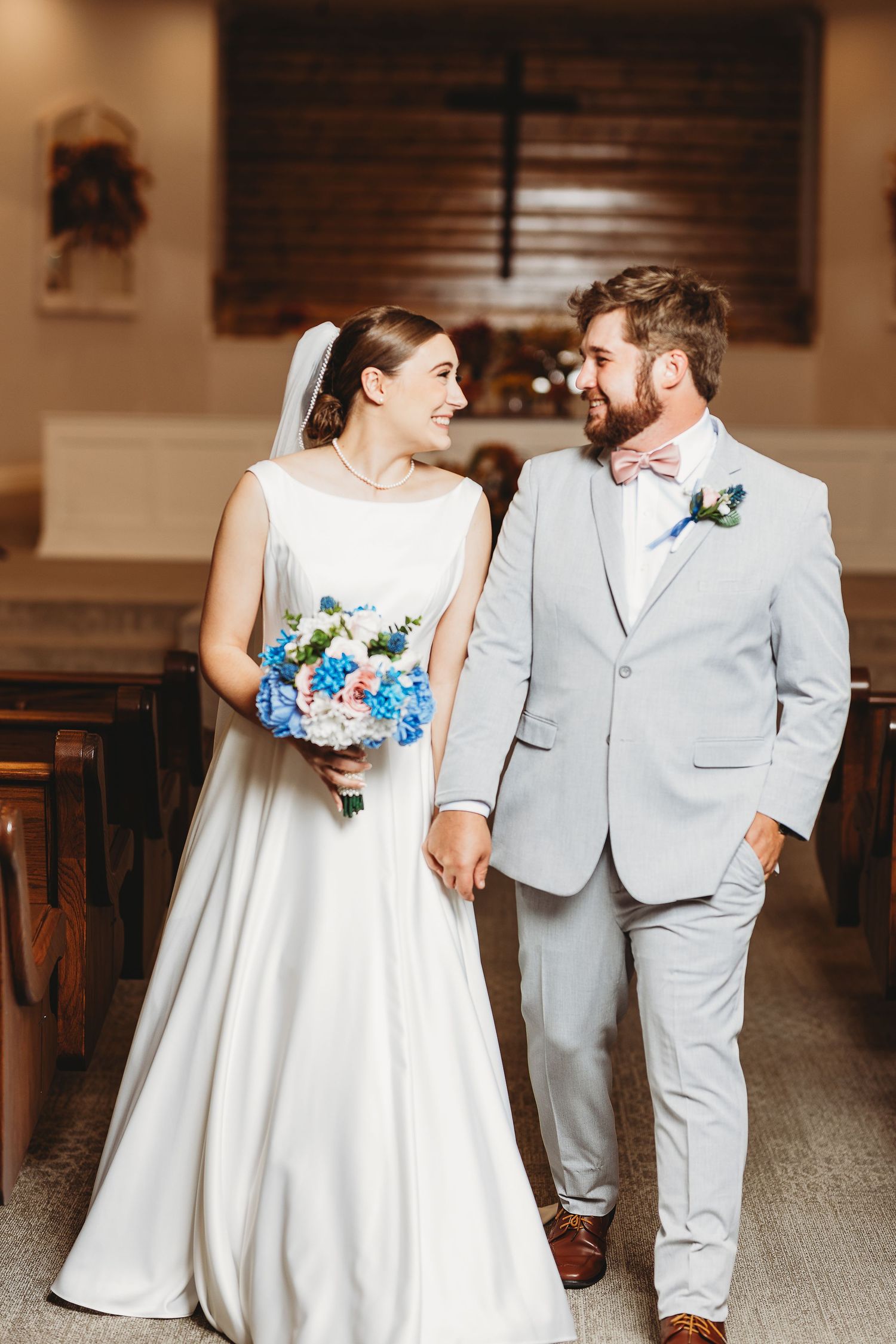 Wedding couple shares intimate moments in a church hallway wearing white dress and light gray suit.