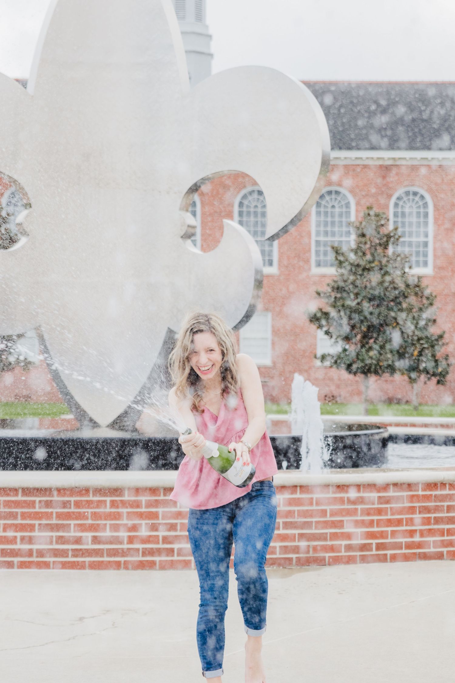 A playful pose in front of a large fleur-de-lis sculpture on a brick building.
