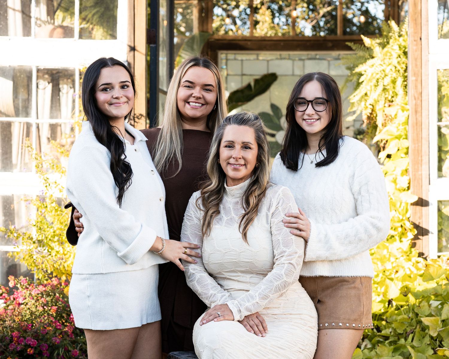 A group in coordinated white and brown outfits poses together outdoors in front of a building with autumn foliage.
