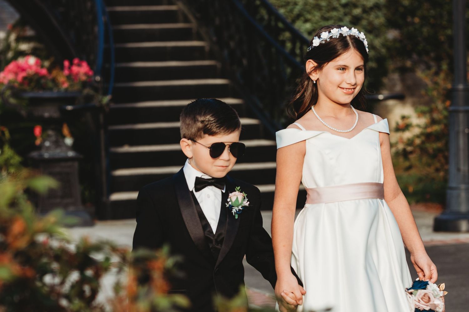 Wedding party members in formal attire pose on outdoor steps with floral decorations.