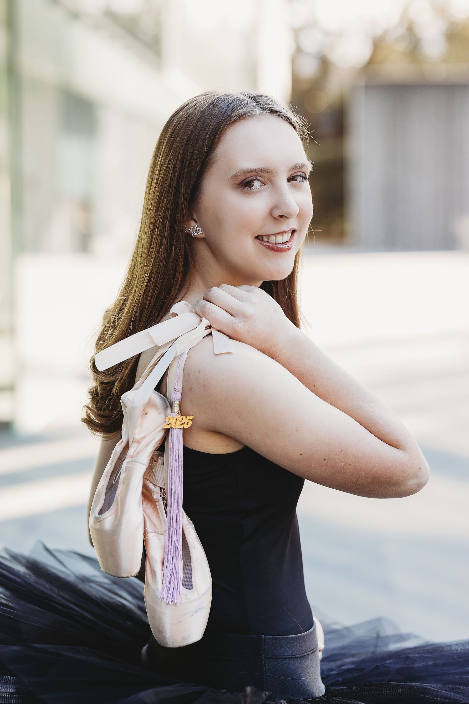 A ballet dancer holds pointe shoes while wearing a black leotard and tutu.