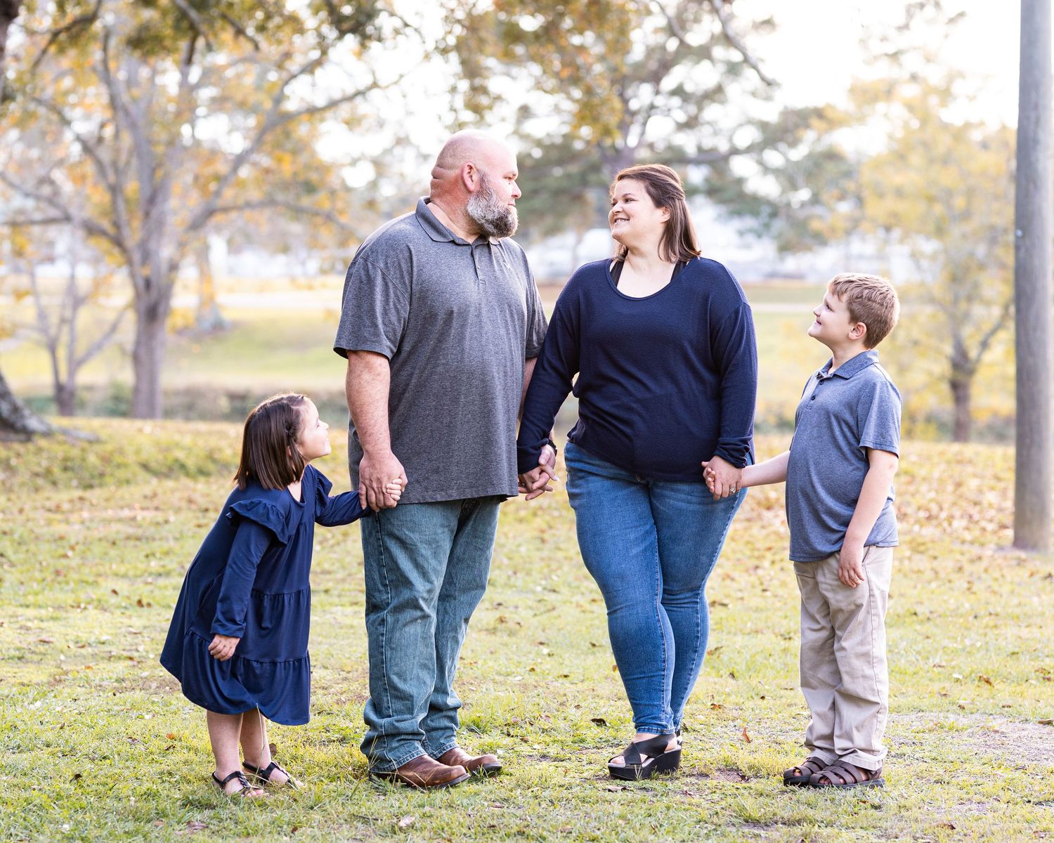 A family of four enjoying a candid moment together in a park setting.