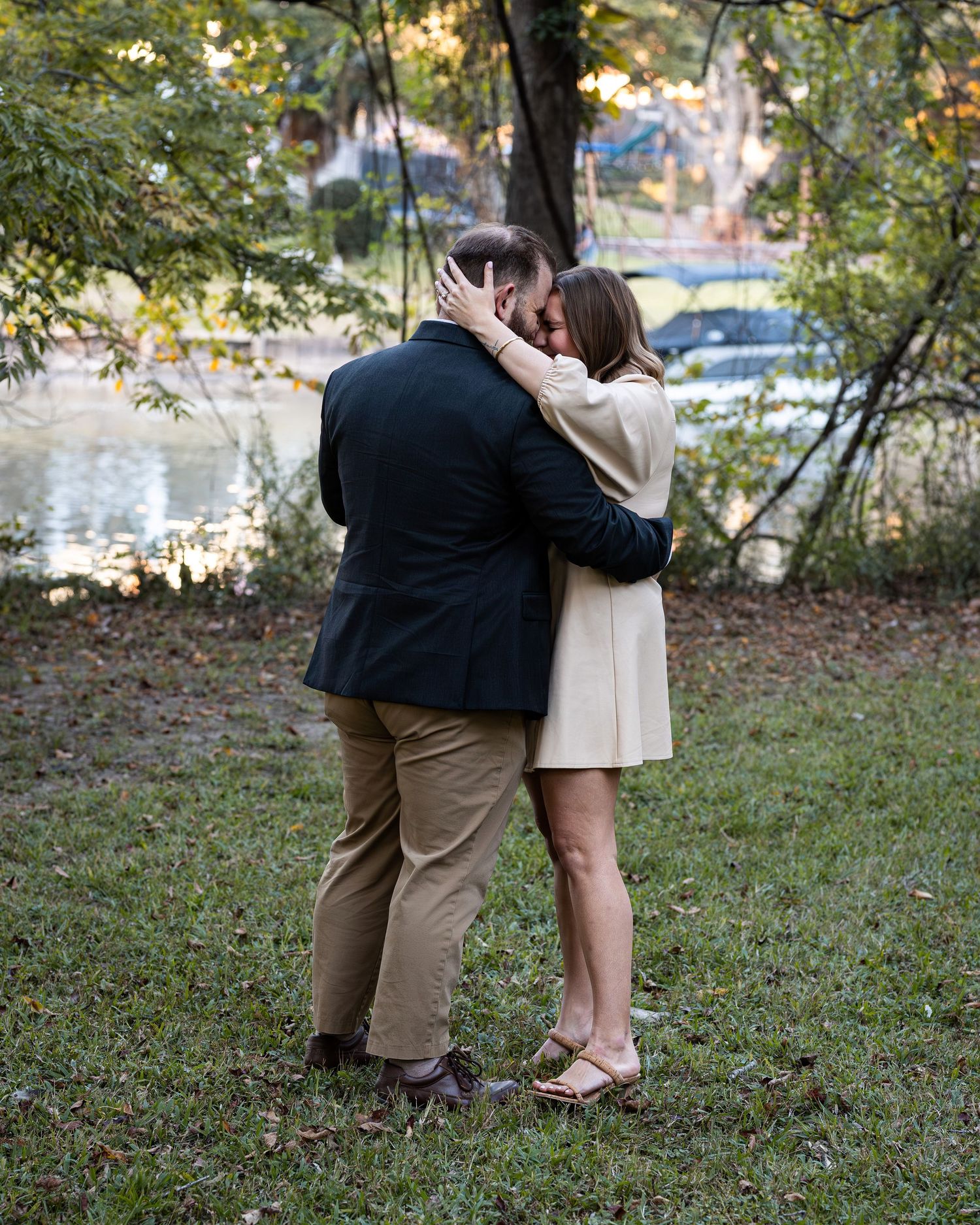 A couple shares a tender embrace in a wooded outdoor setting during autumn.