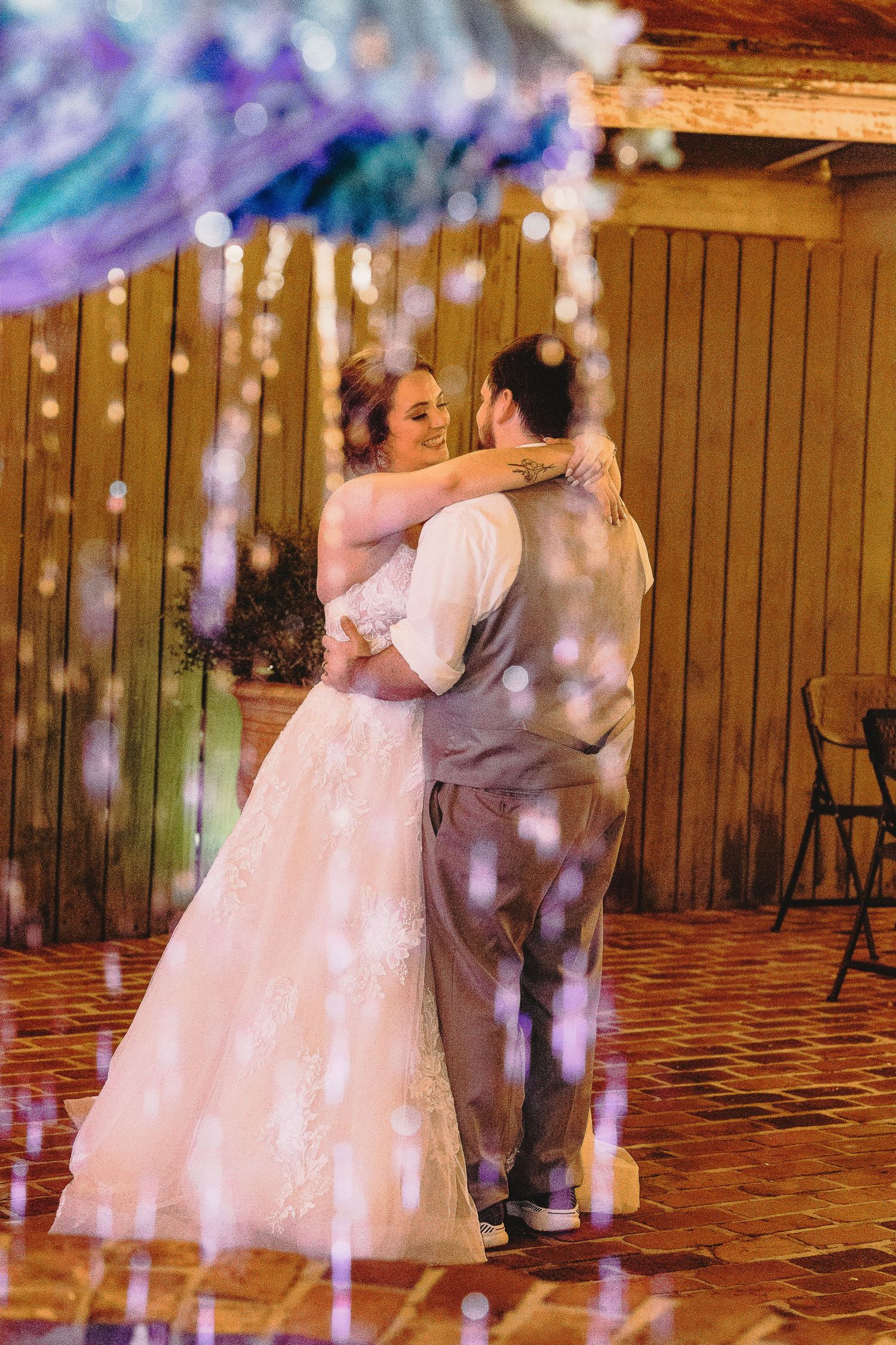 A couple dances in soft purple lighting with string lights creating a magical atmosphere.