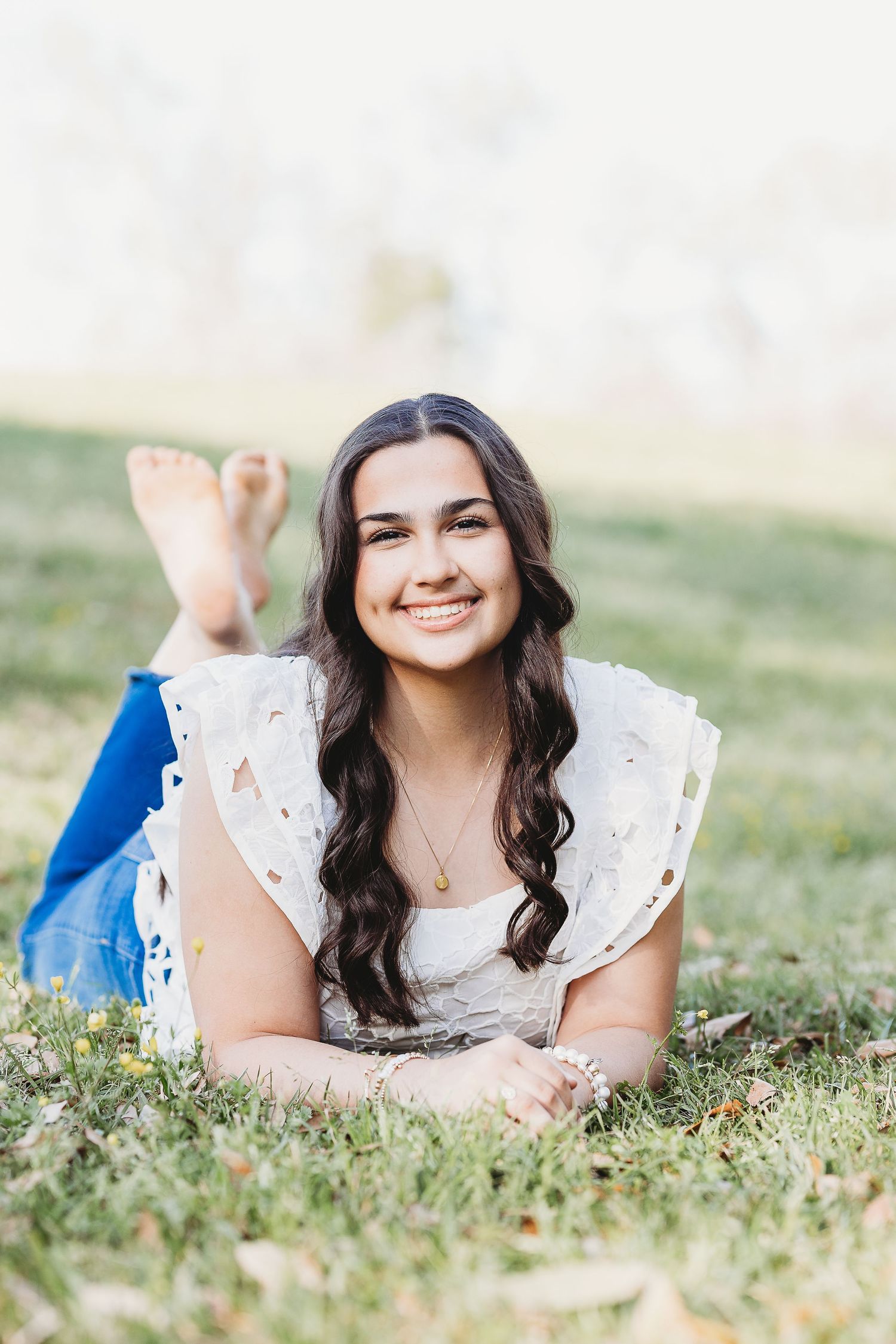 Person in white eyelet dress lies on grass during spring photo session.