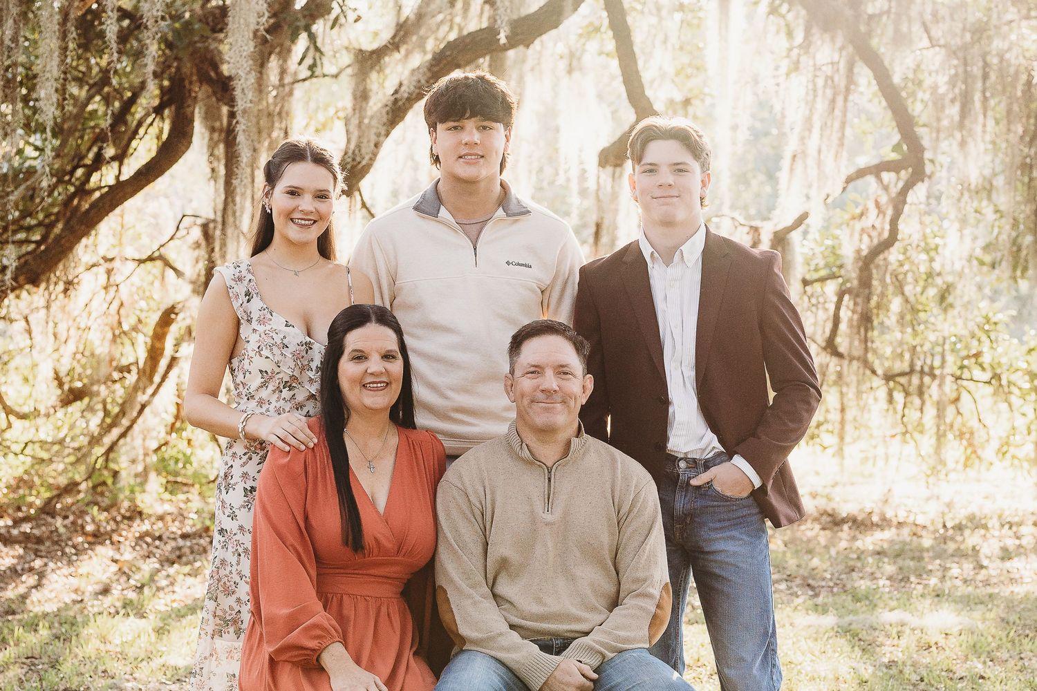 Five people gather for a family portrait under moss-covered trees in natural lighting.