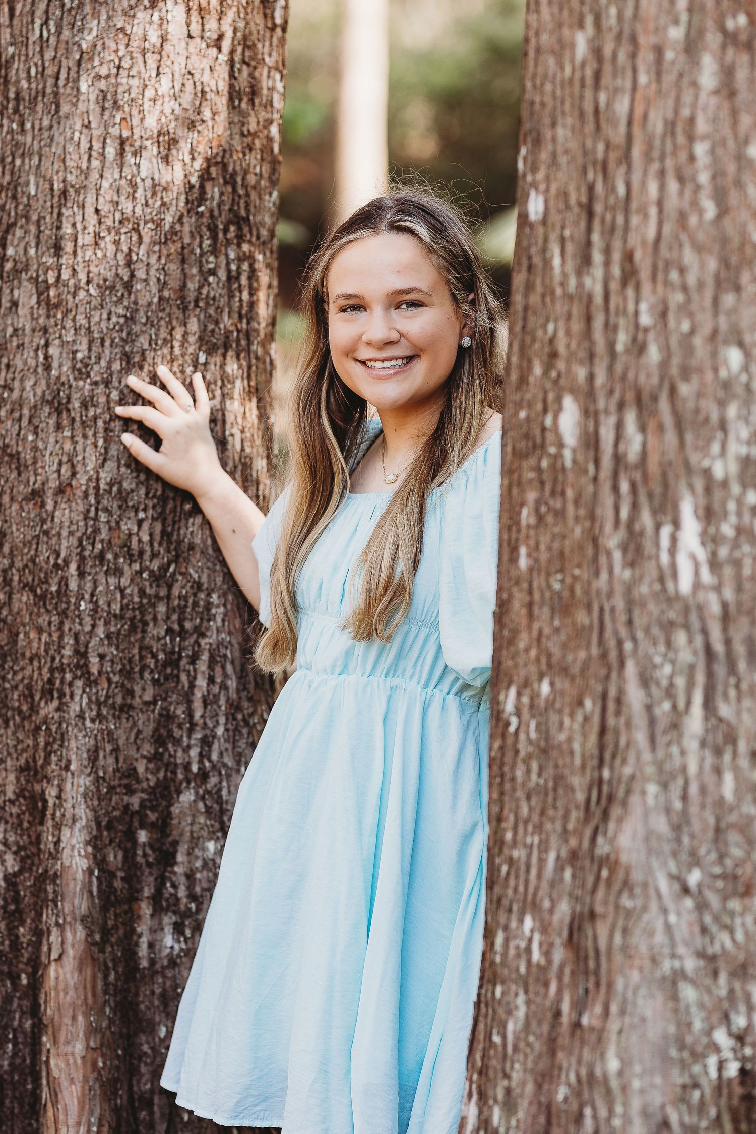 Outdoor portrait series against rustic tree bark wearing a flowing light blue dress.