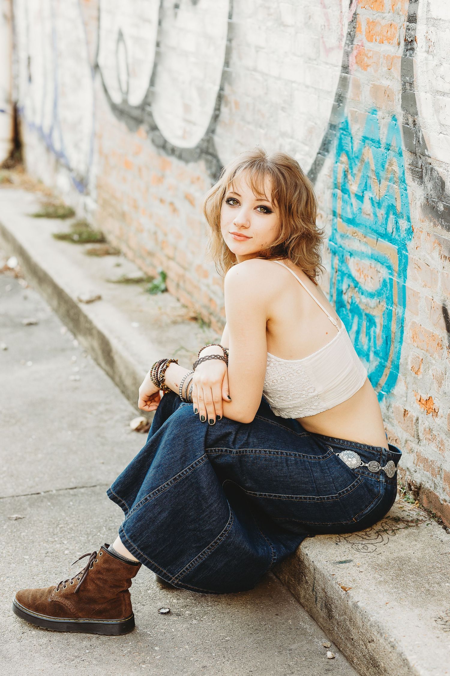 Urban fashion portrait of model in crop top and jeans sitting against graffiti wall.