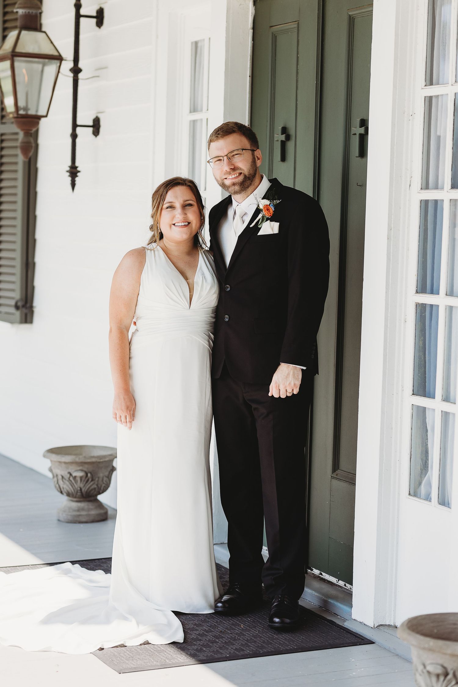 Wedding couple poses on an elegant white porch with classic lanterns and architectural details.