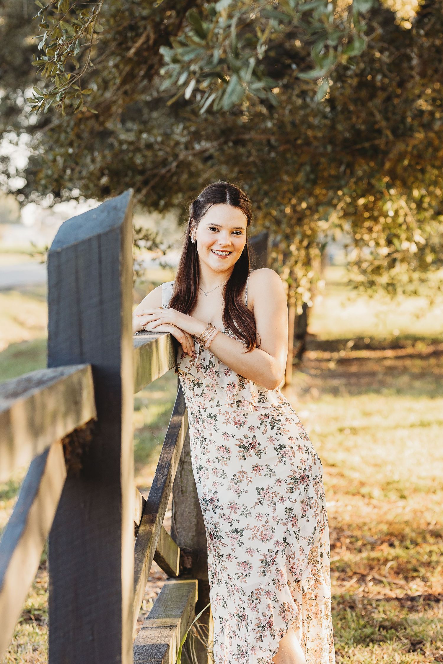 Portrait series in floral dress near wooden fence during golden hour.