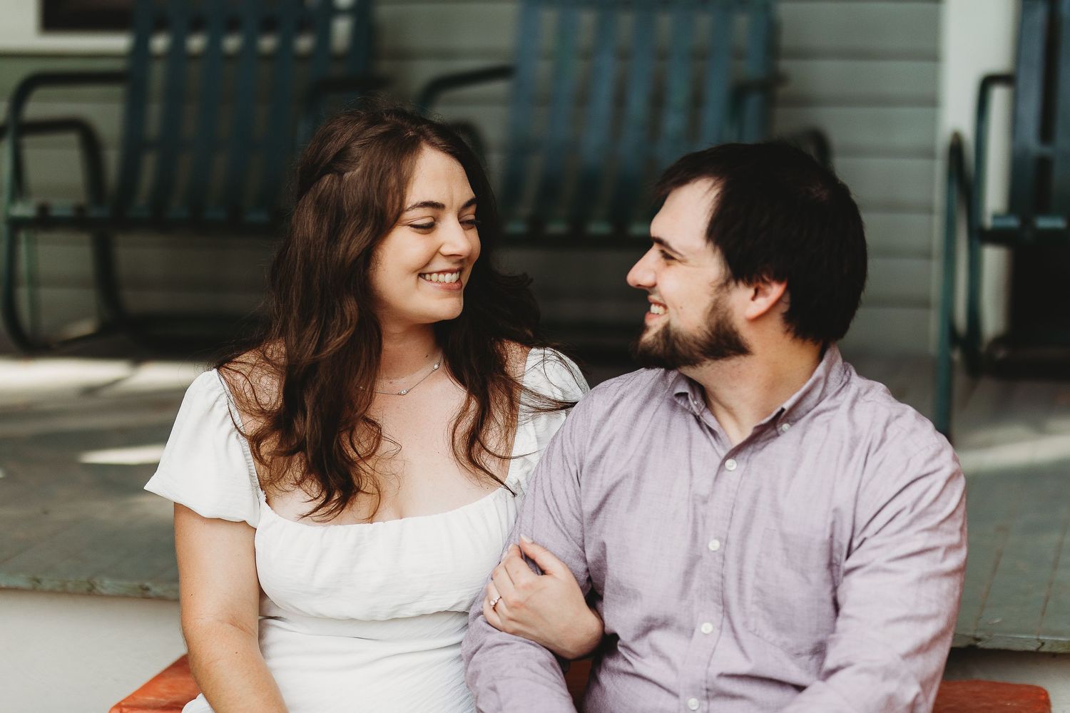 A romantic couple shares intimate moments while sitting on a porch in casual attire.