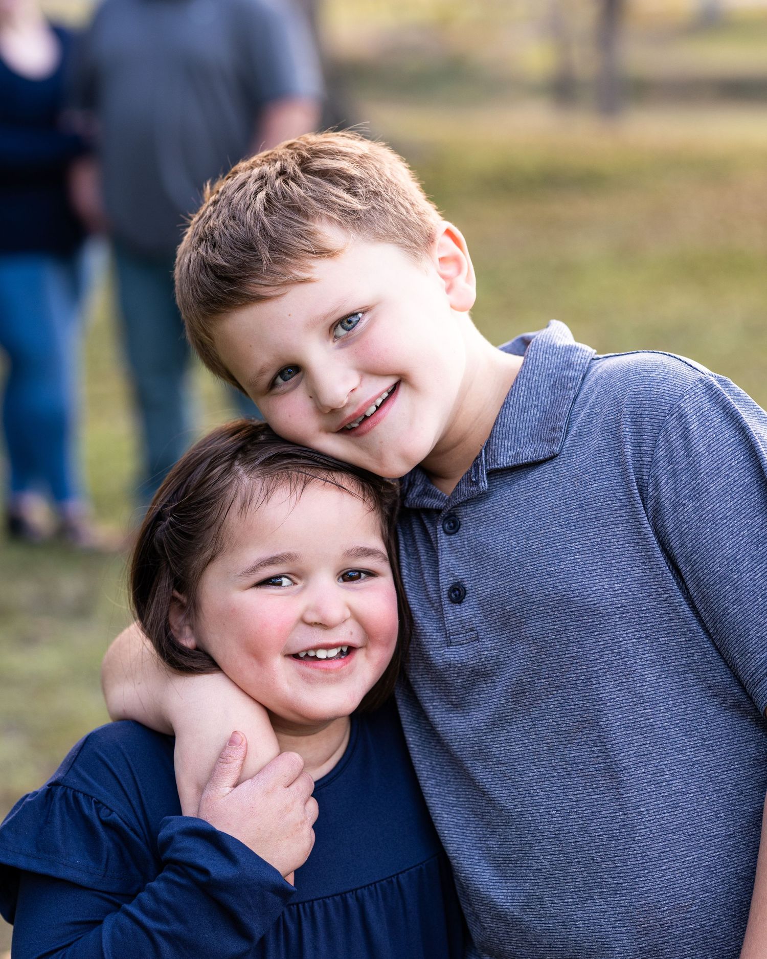 Two young children in casual clothing sharing a playful moment together outdoors on a sunny day.