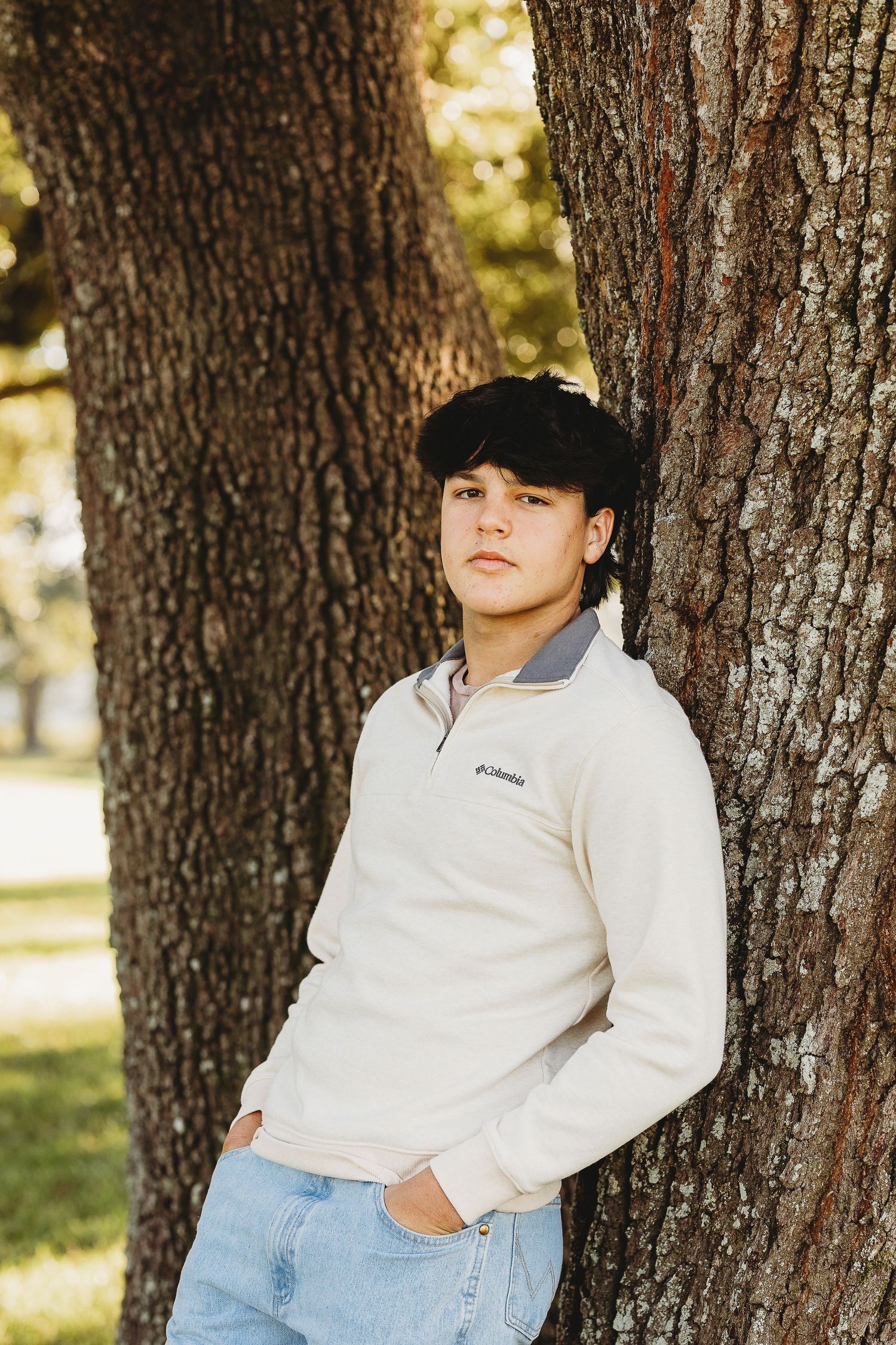 Casual portrait series leaning against tree trunks in white top and jeans.