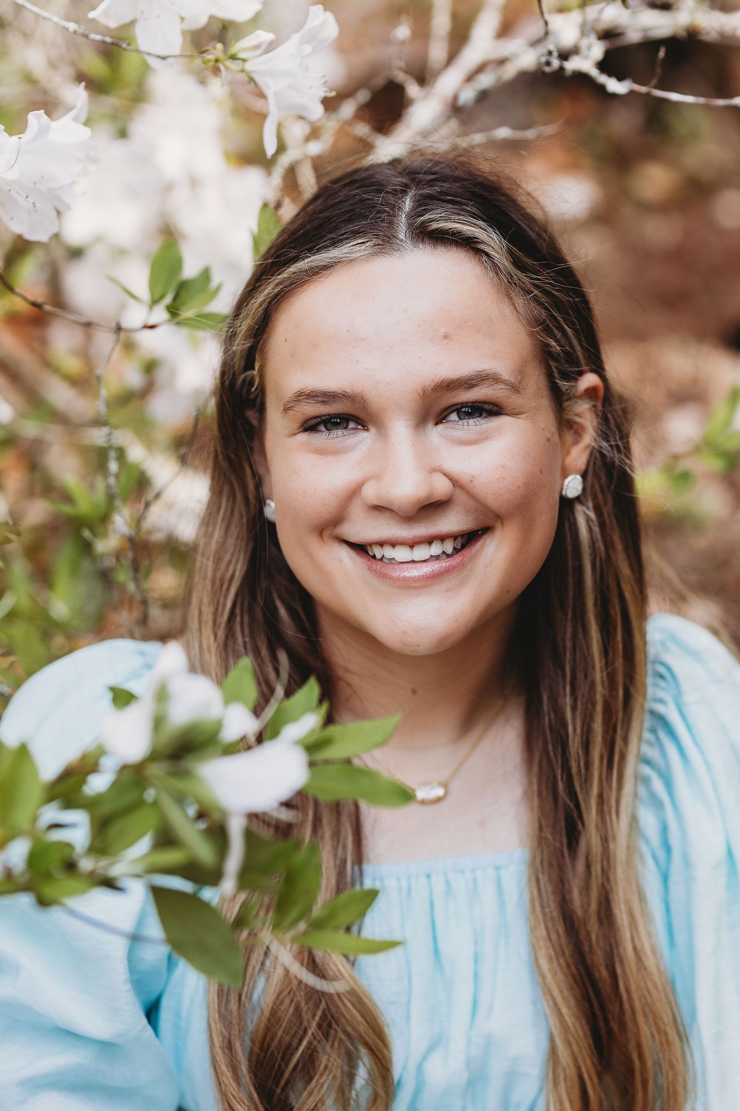Portrait series in a natural setting with white flowers and light blue dress against a blurred background.