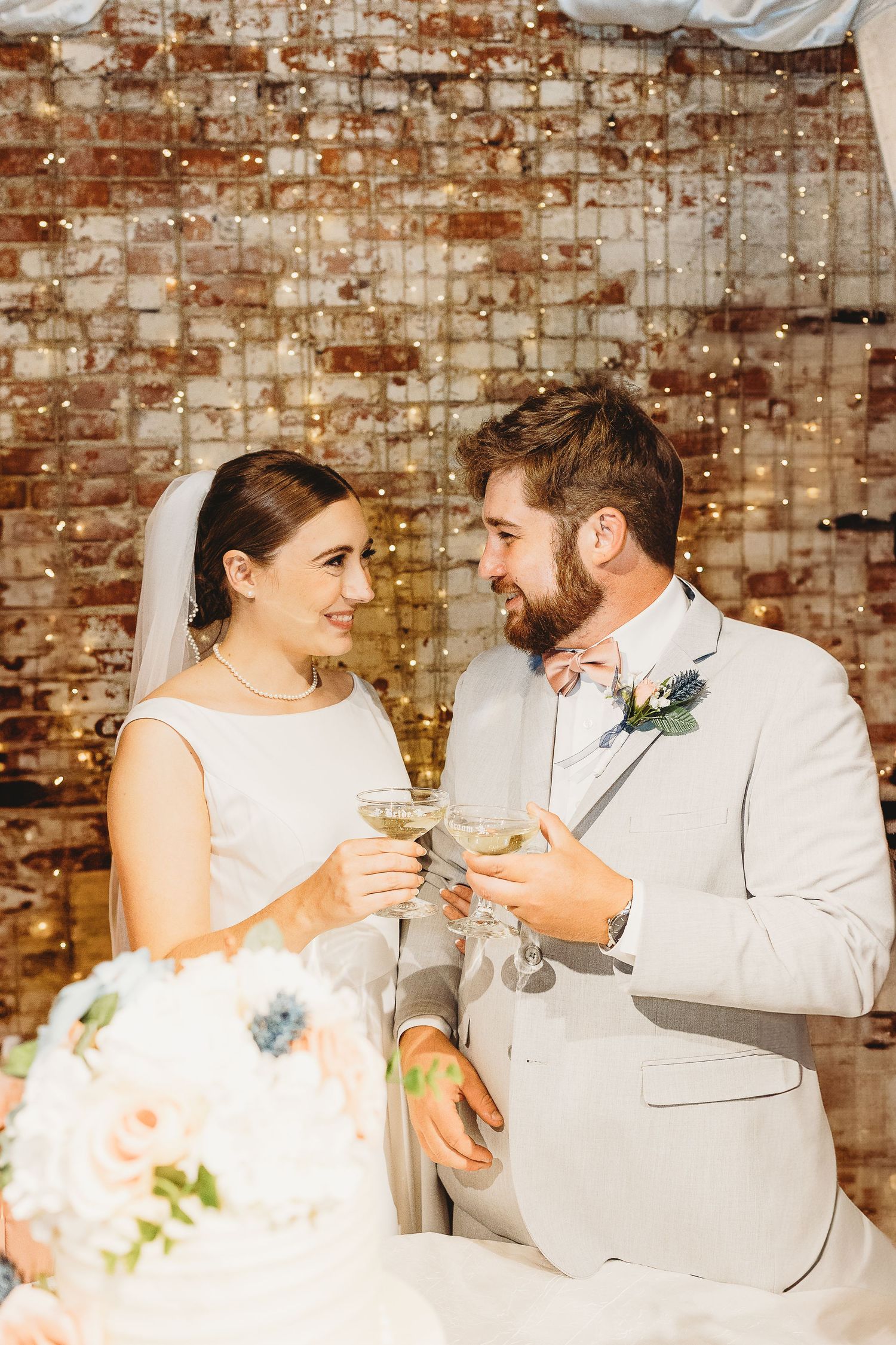 Couple shares intimate moment with champagne glasses against rustic brick wall backdrop.