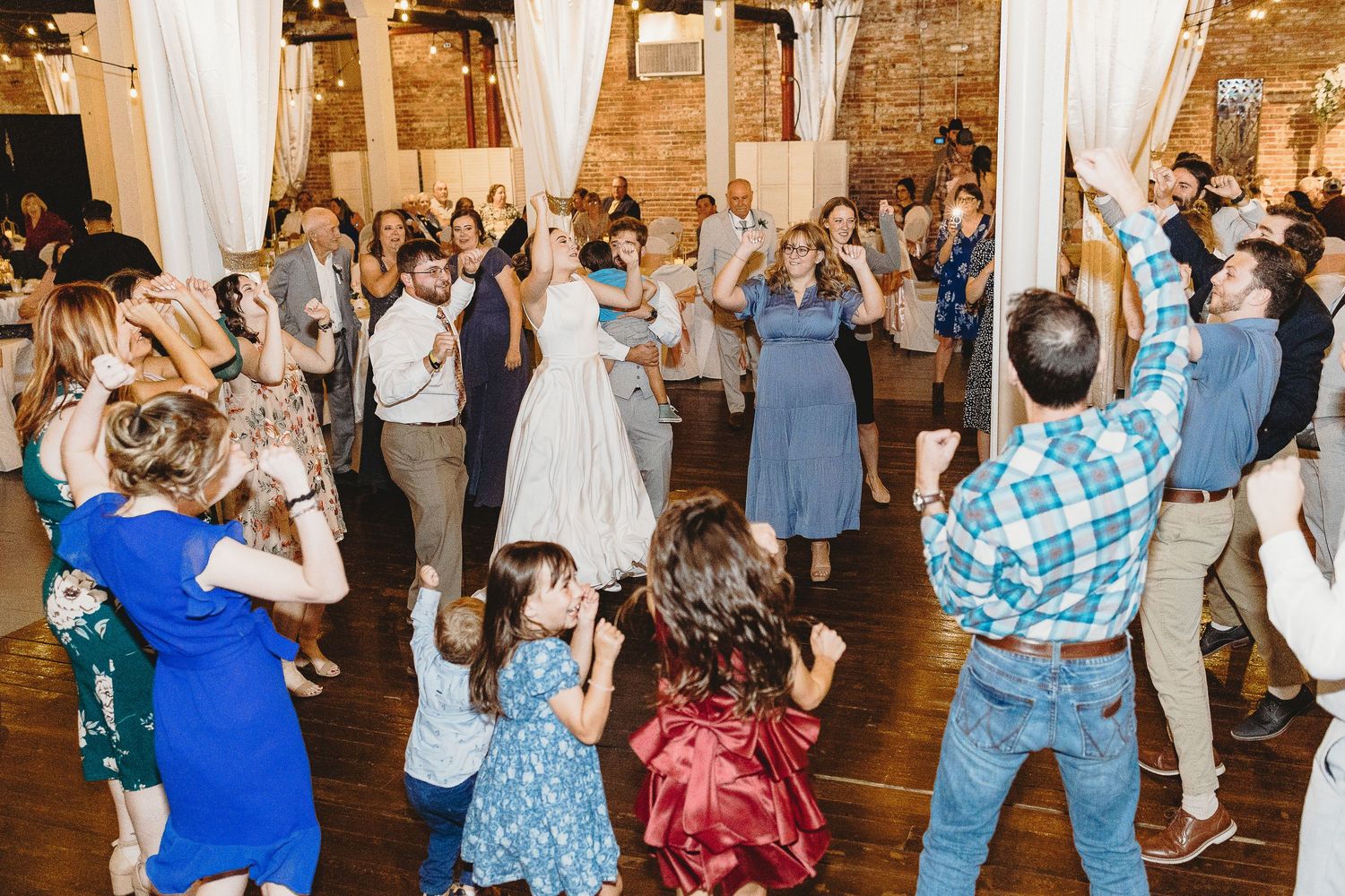 Wedding reception dance floor filled with guests celebrating and dancing in a rustic venue.