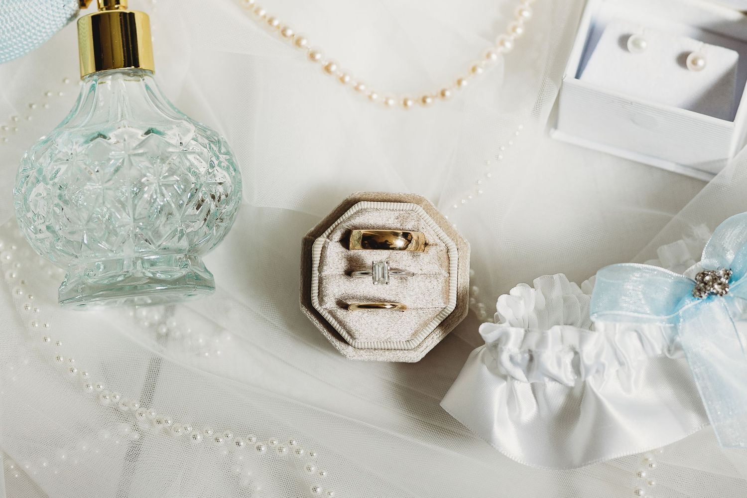 Elegant wedding details with pearls, perfume bottles, and delicate accessories in soft lighting.