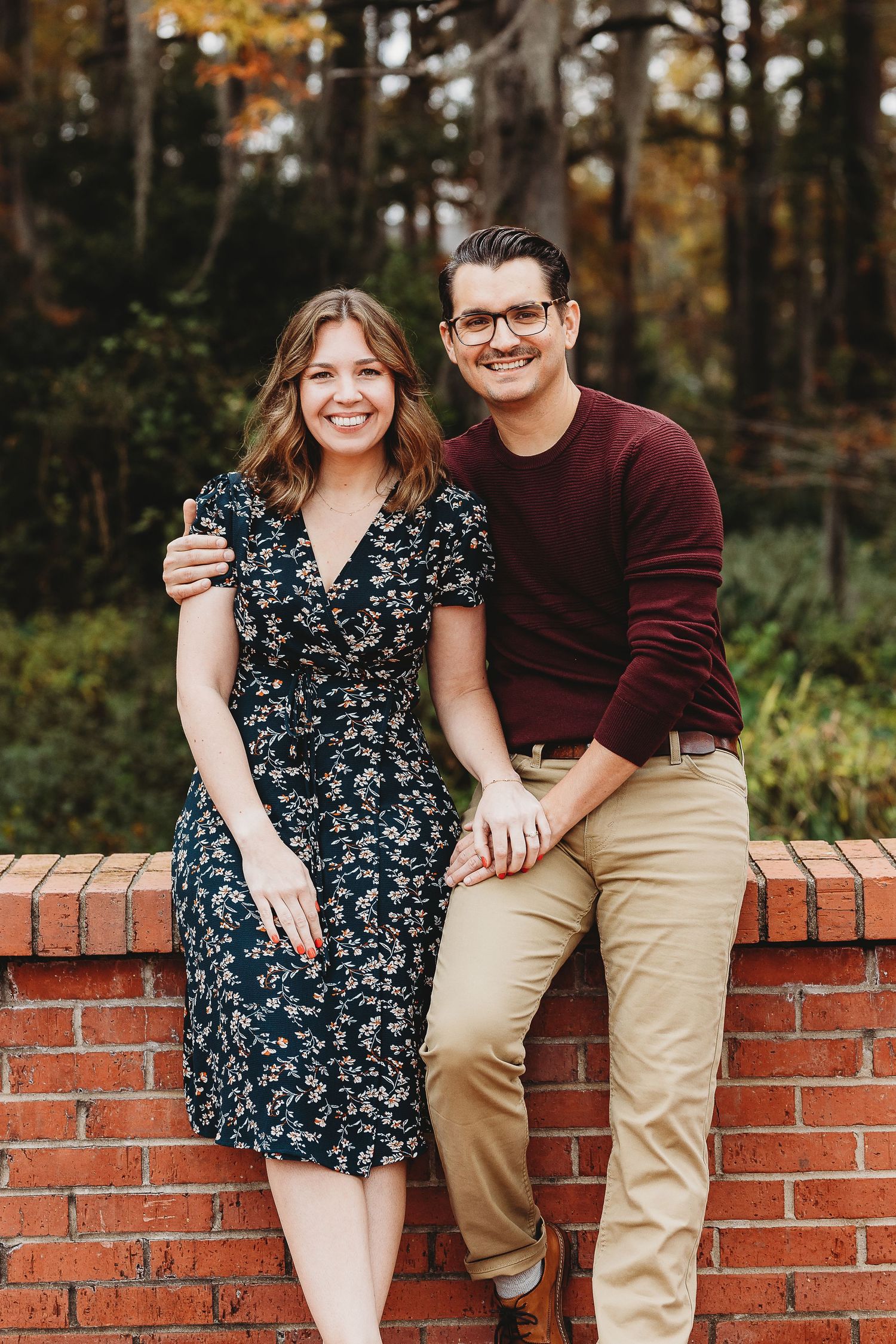 Casual outdoor portraits on a brick wall with autumn trees creating a natural backdrop.