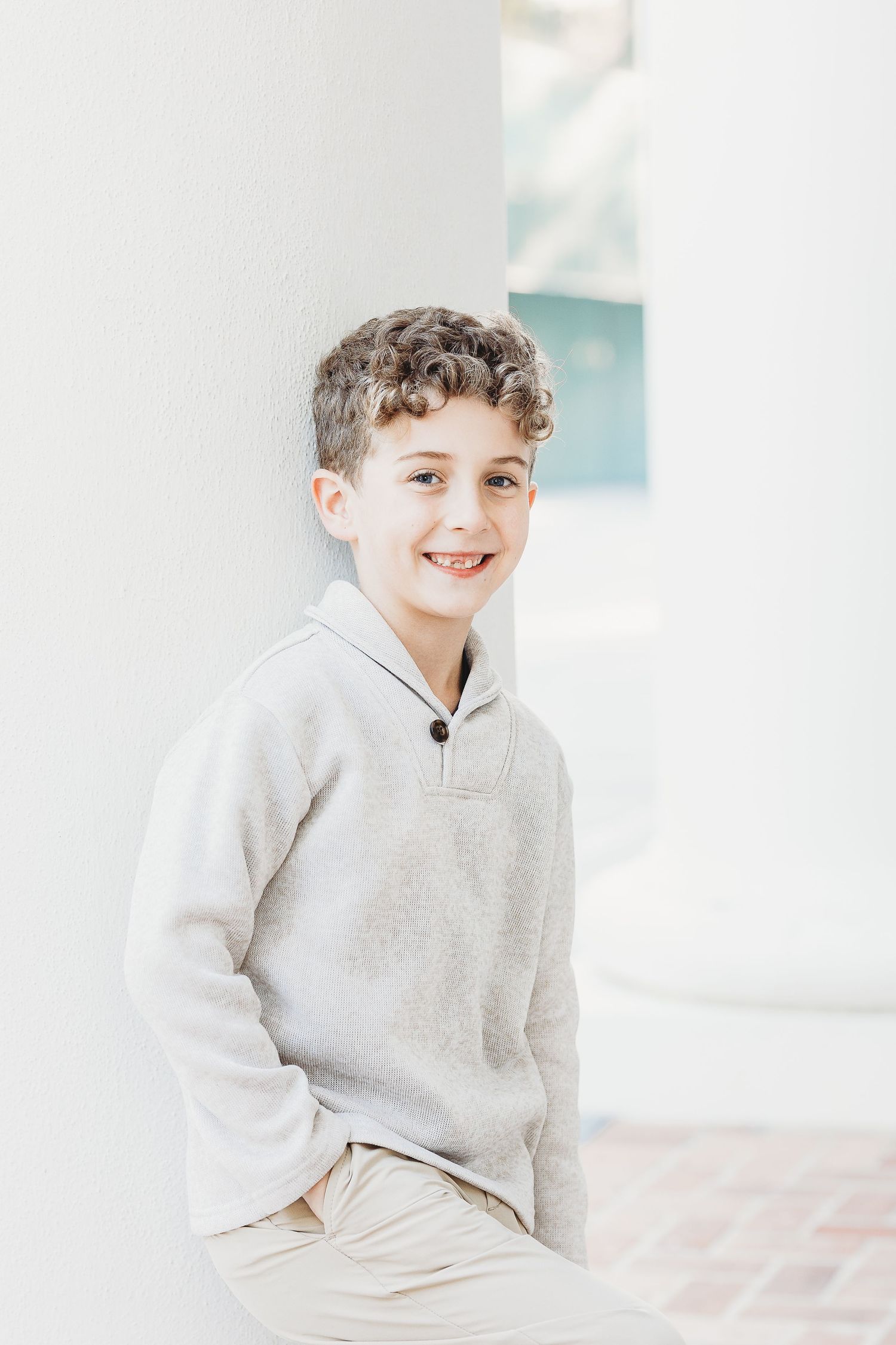 Young person in light gray sweater poses casually against bright white background.
