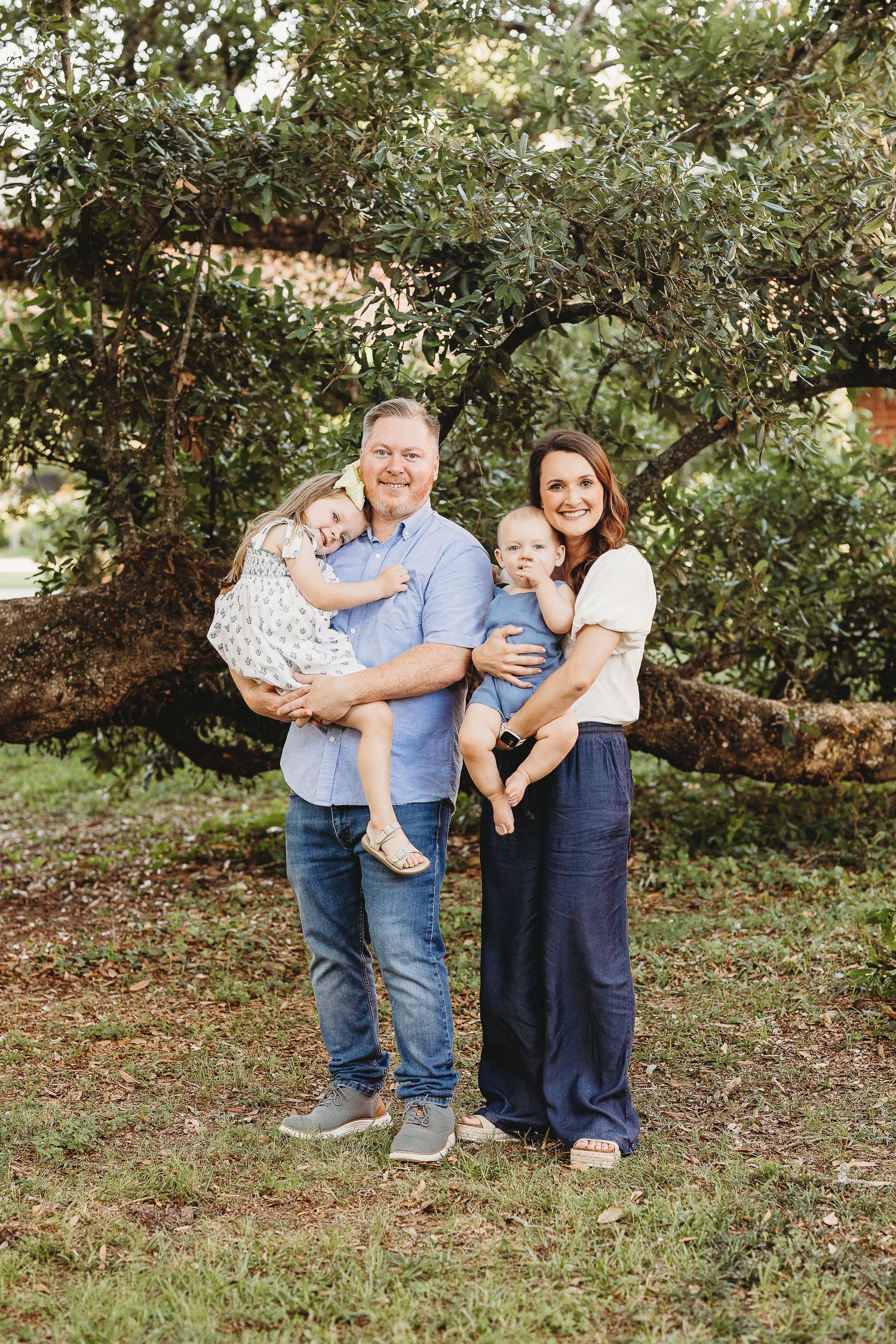 A family poses together under a sprawling tree during a casual outdoor photo shoot.