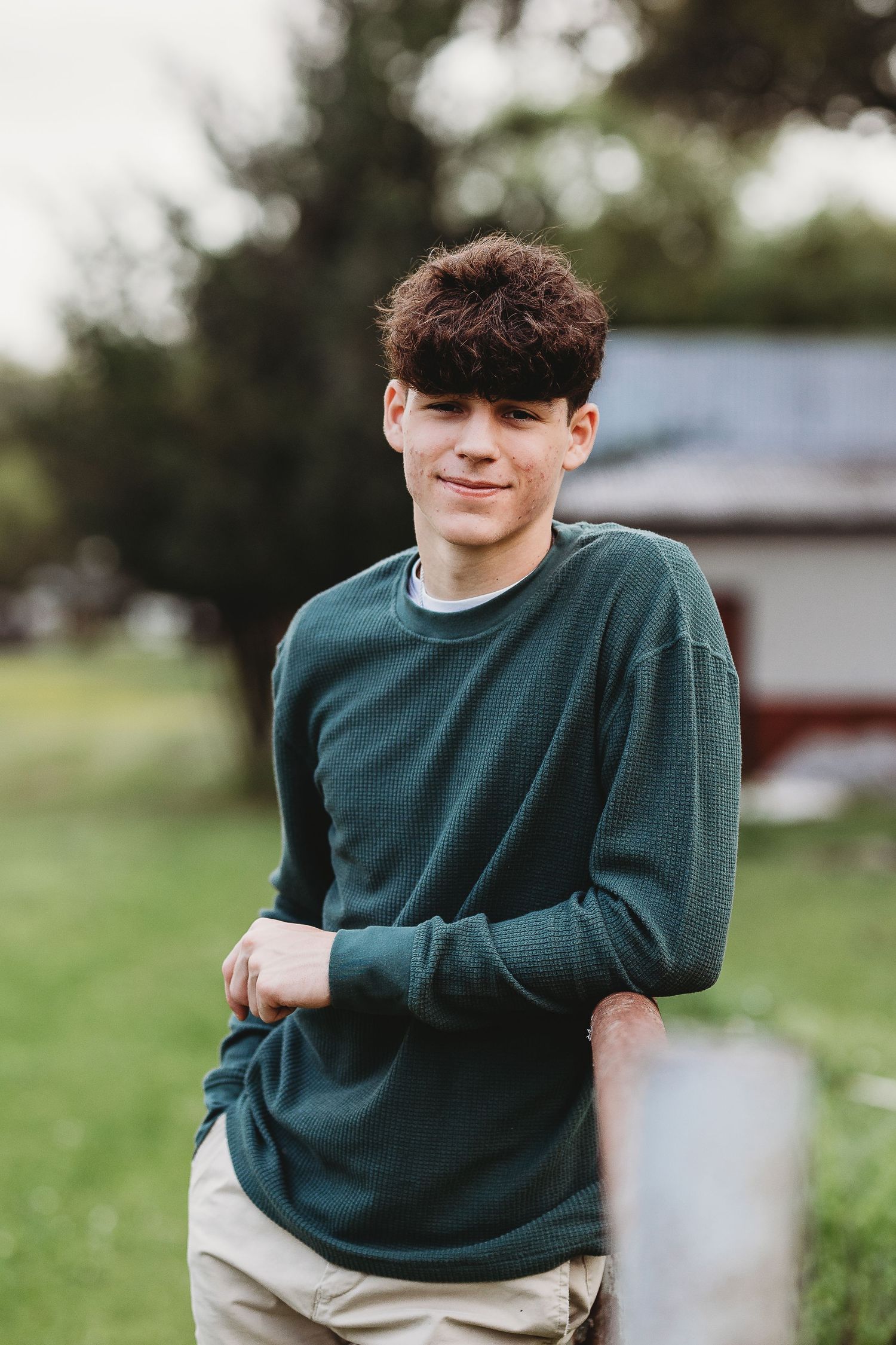 Person wearing dark green sweater poses outdoors in casual portrait session.