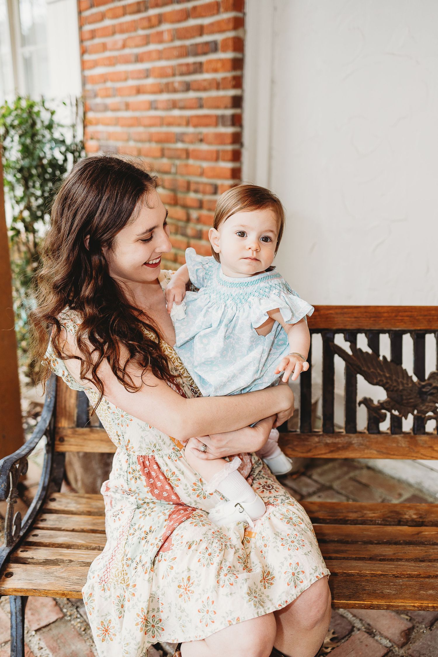 Mother and baby bonding on wooden bench against brick wall interior.