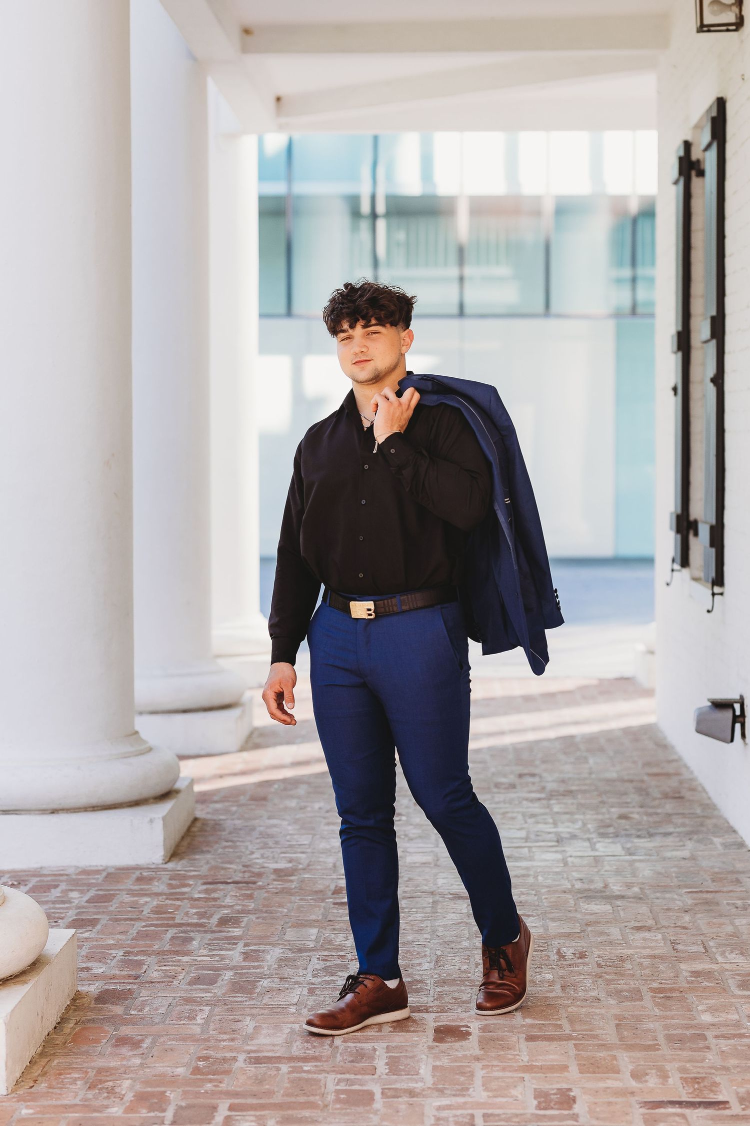 Person in navy suit walking through white columned walkway with brick floor.