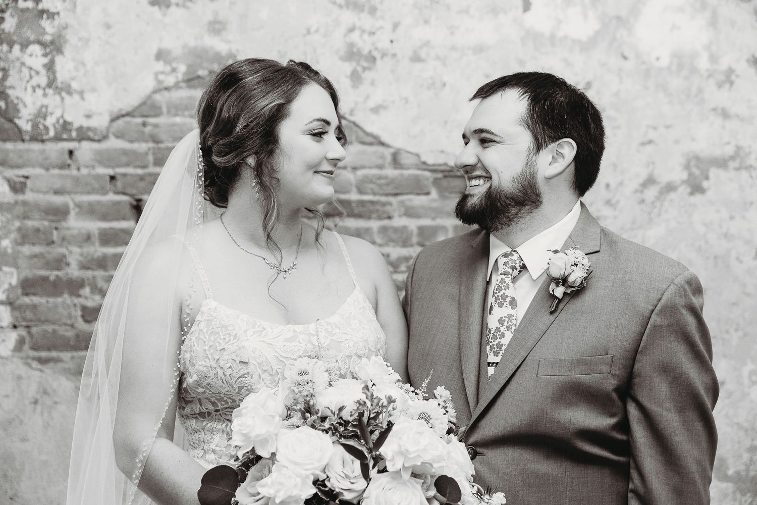 Wedding couple sharing a romantic moment against a vintage brick and plaster wall.