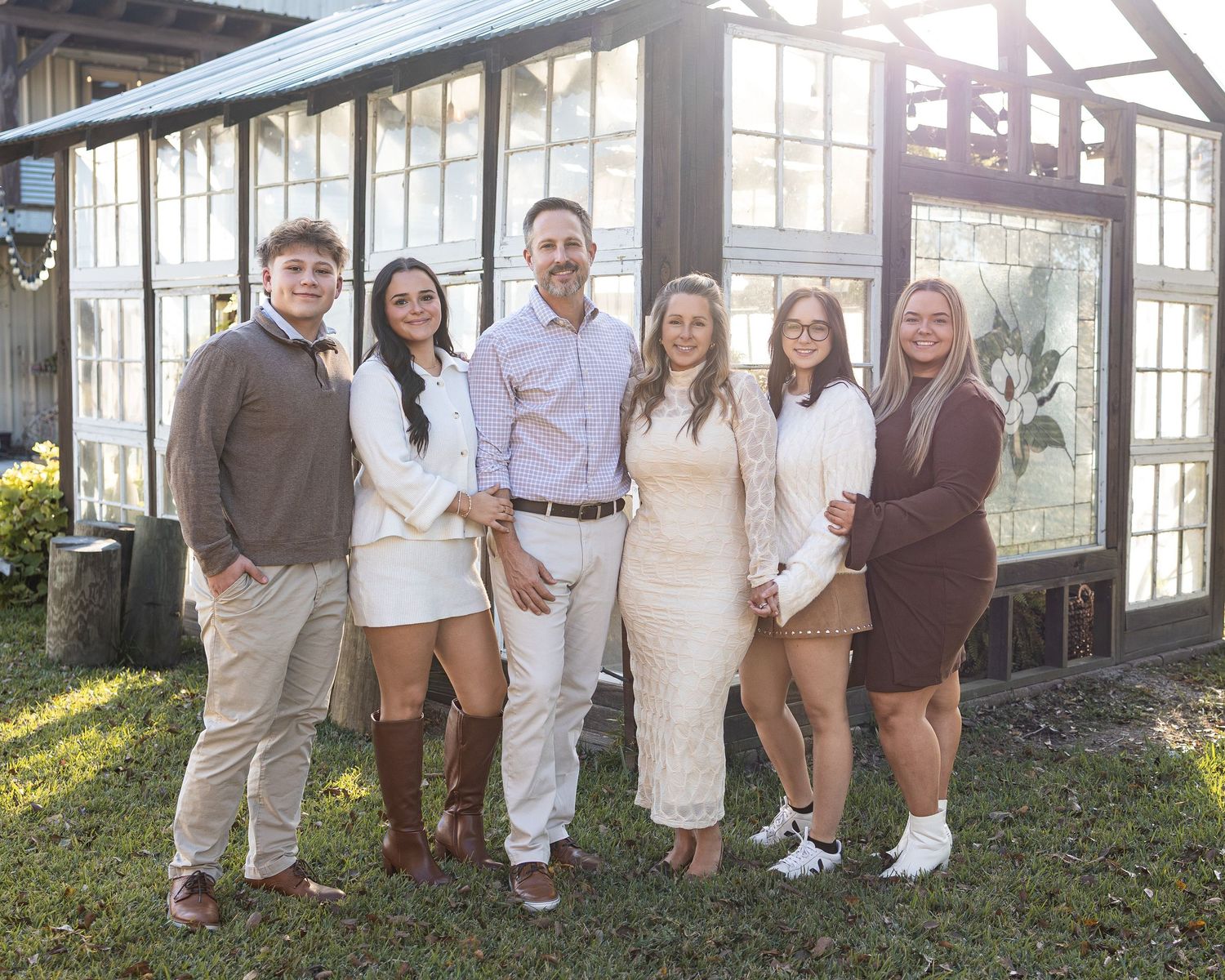 A family group poses together outdoors wearing coordinated white and brown outfits for a casual portrait session.
