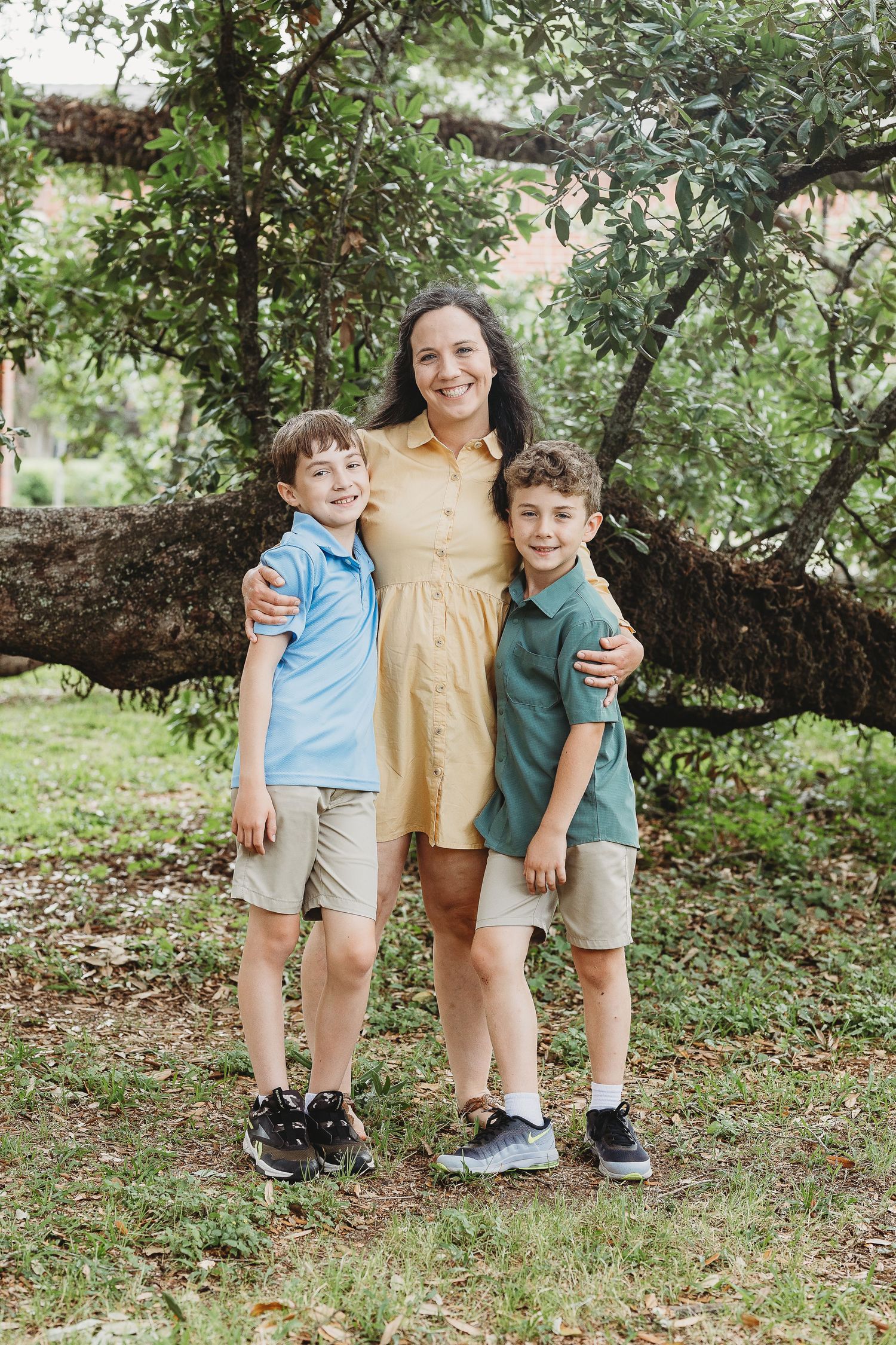 A casual outdoor family portrait session showing playful poses under a shady tree.