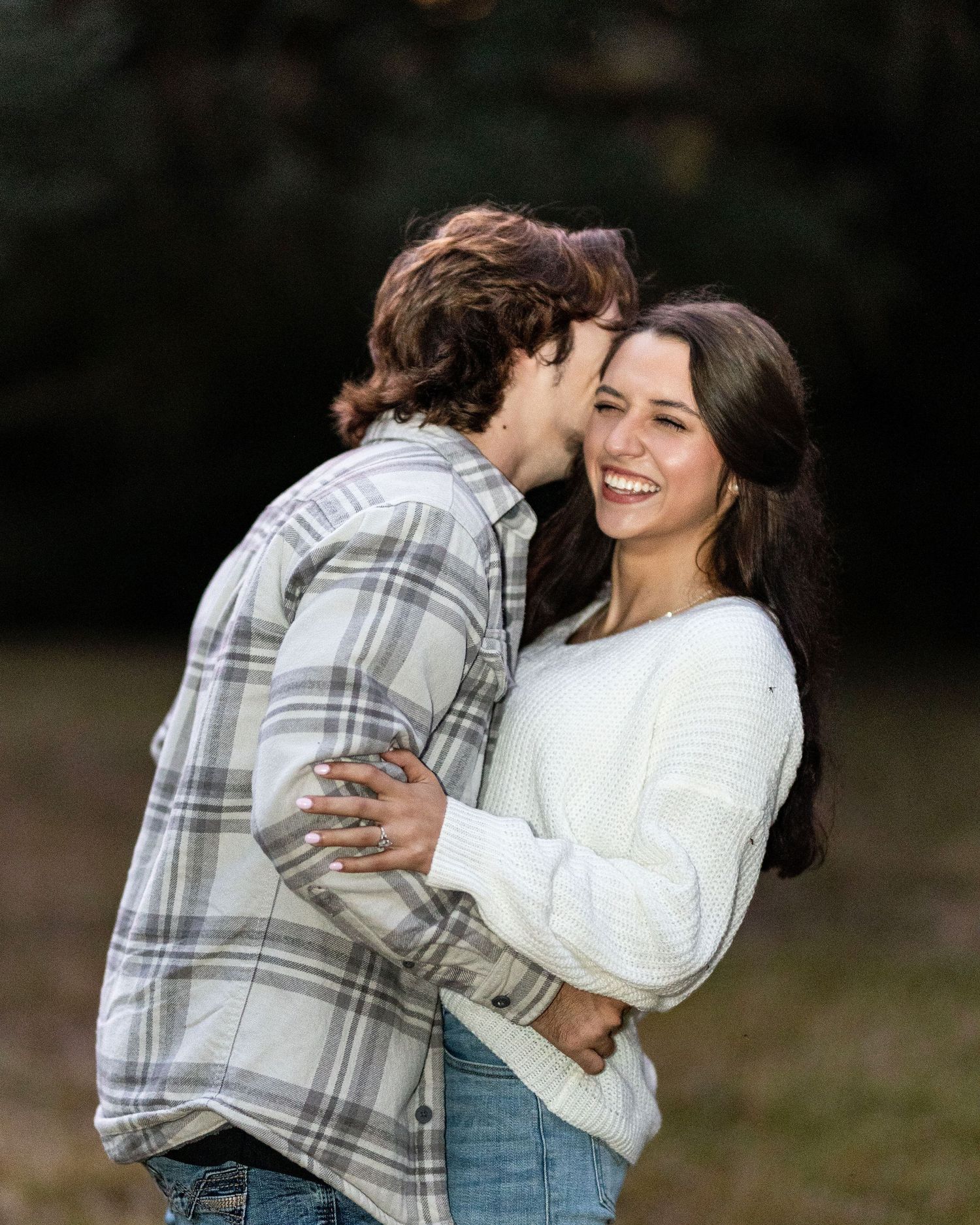A joyful candid moment between a couple laughing and embracing outdoors in casual fall attire.