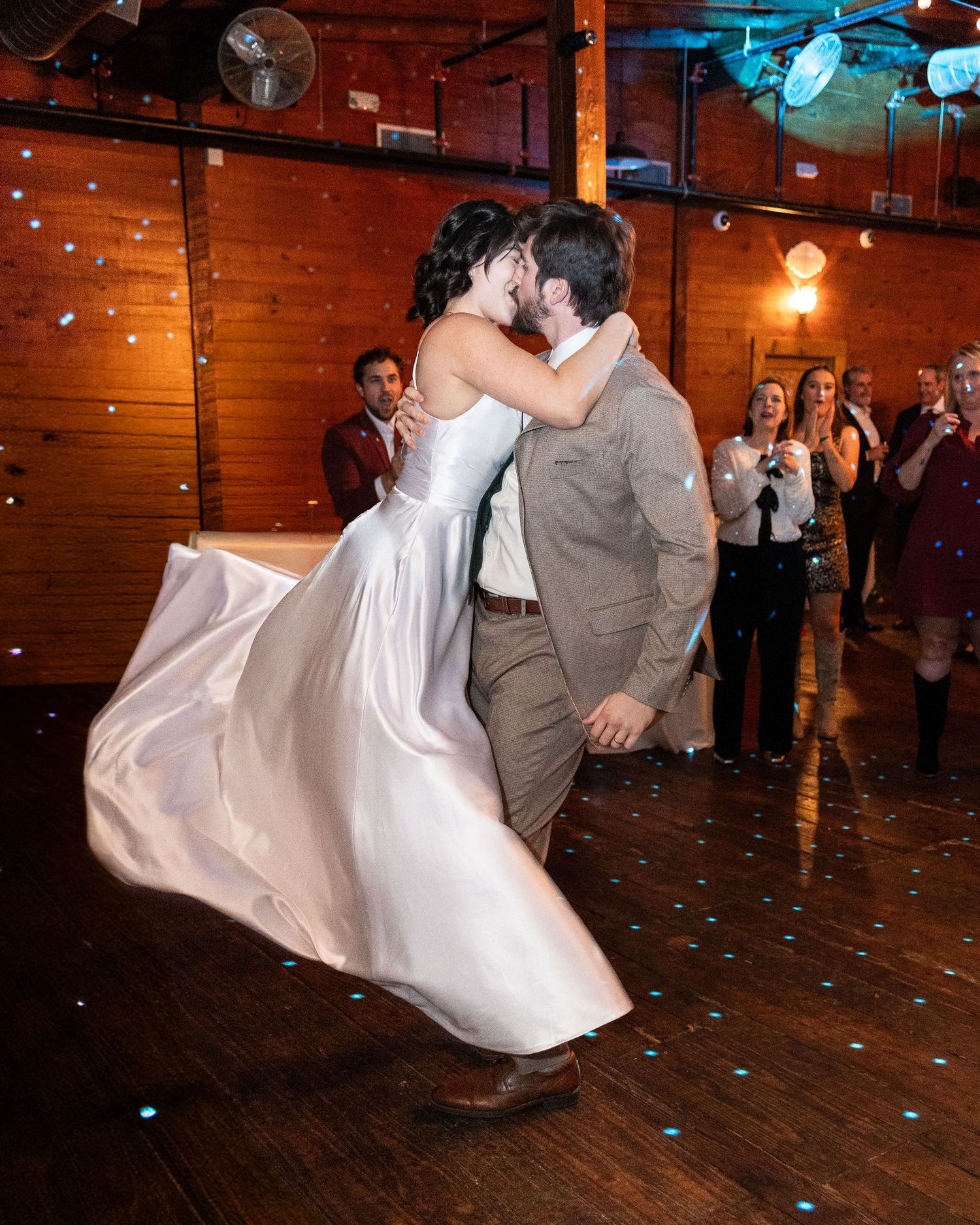 A couple performs a dramatic dance dip move during their first dance at a rustic barn wedding reception.