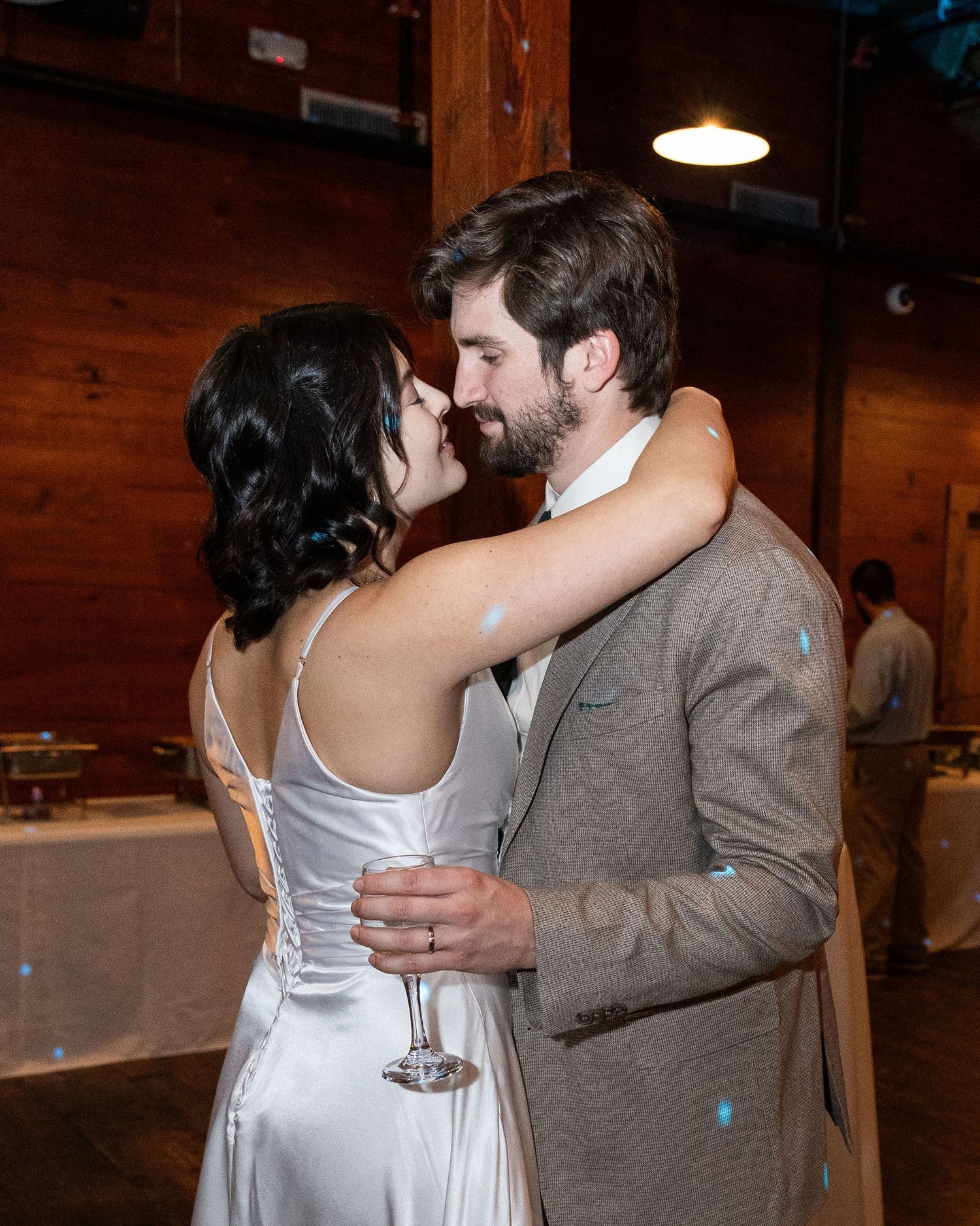 A couple in a rustic venue share a romantic dance together, with the person in white wearing a flowing dress.