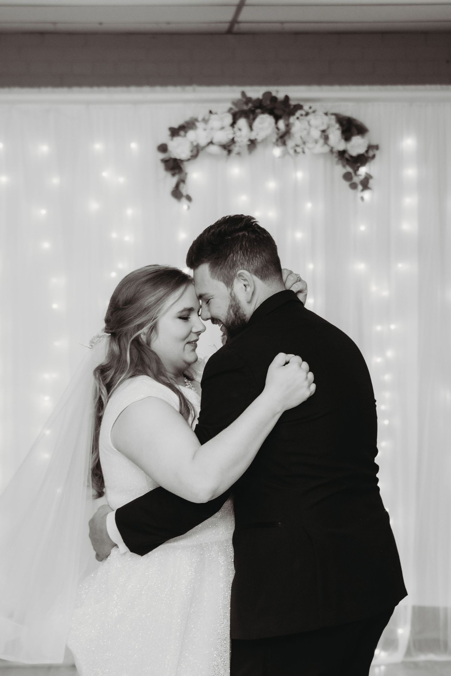 Romantic first dance moment against a white backdrop with twinkling fairy lights.