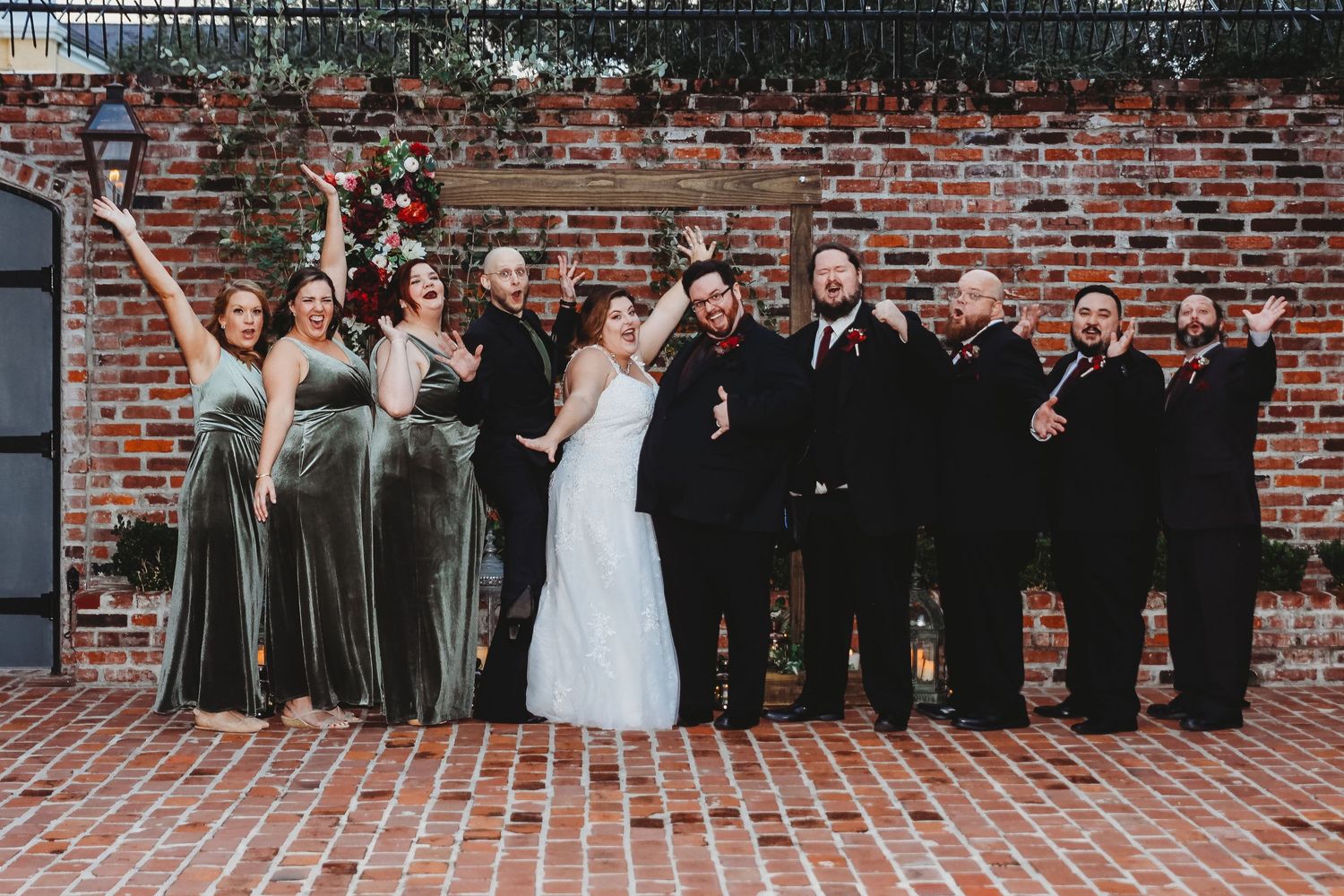 Wedding party lined up against brick wall for formal group photo.