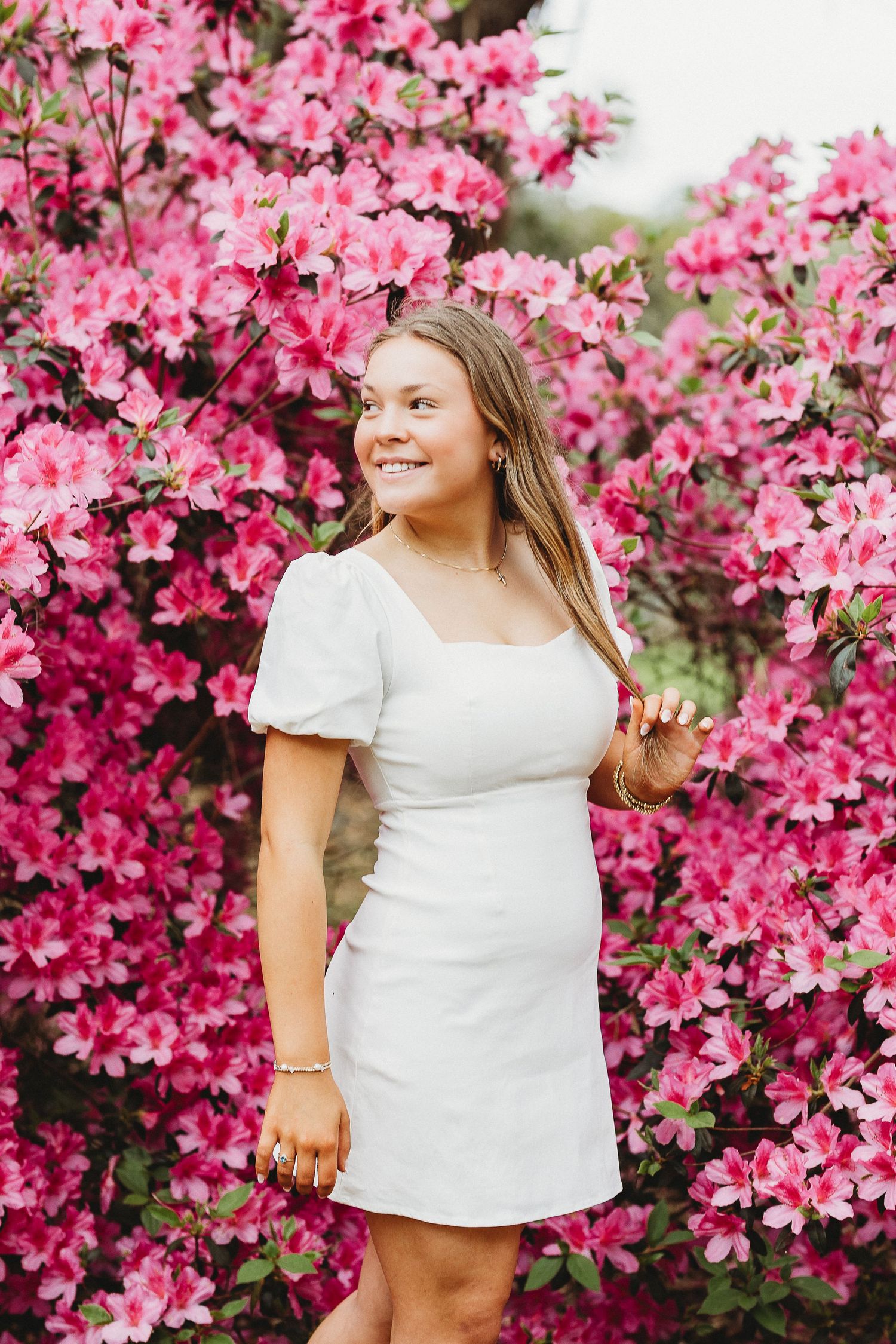Person in white top poses against vibrant pink azalea flowers in full bloom.
