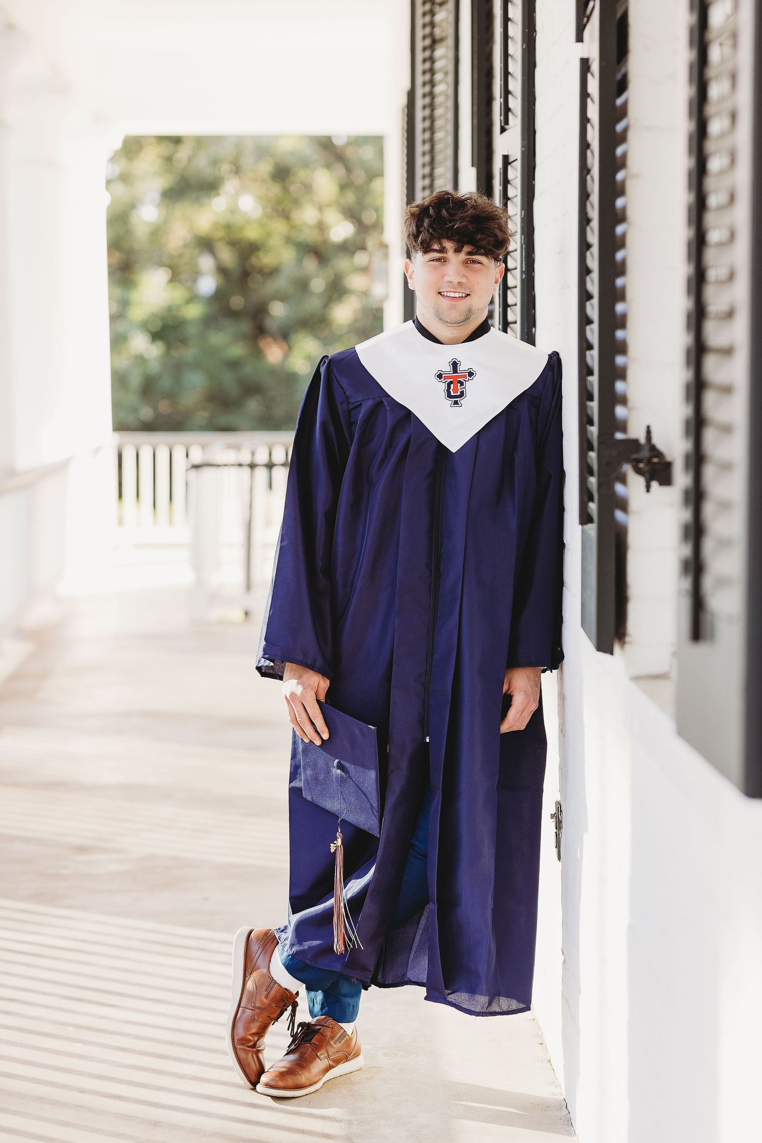 Graduate in navy blue academic regalia poses on a white porch.